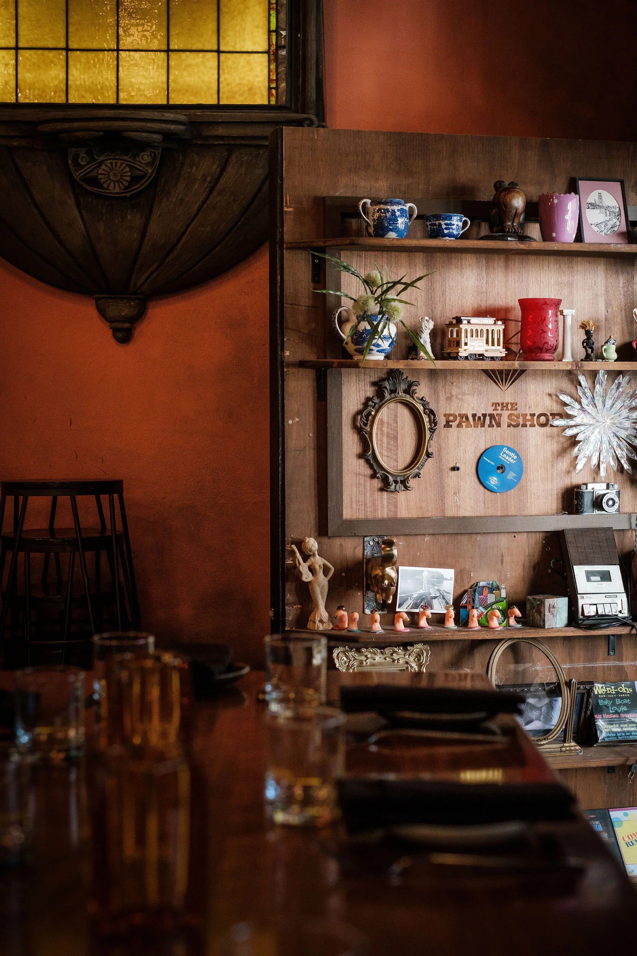 Interior of a cozy establishment with a wooden shelf decorated with various knick-knacks, a mirror, and a toy train, all against a warm-colored wall.