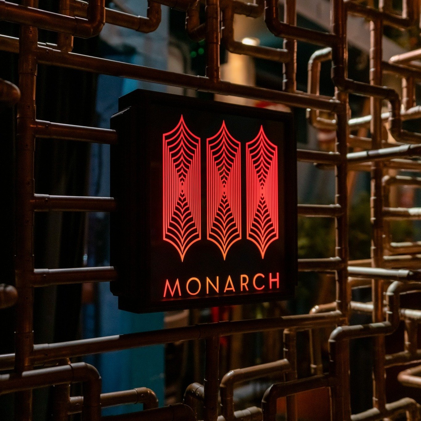 The Monarch neon sign with a red spiderweb pattern and the word 'MONARCH' underneath, mounted on a metal framework.