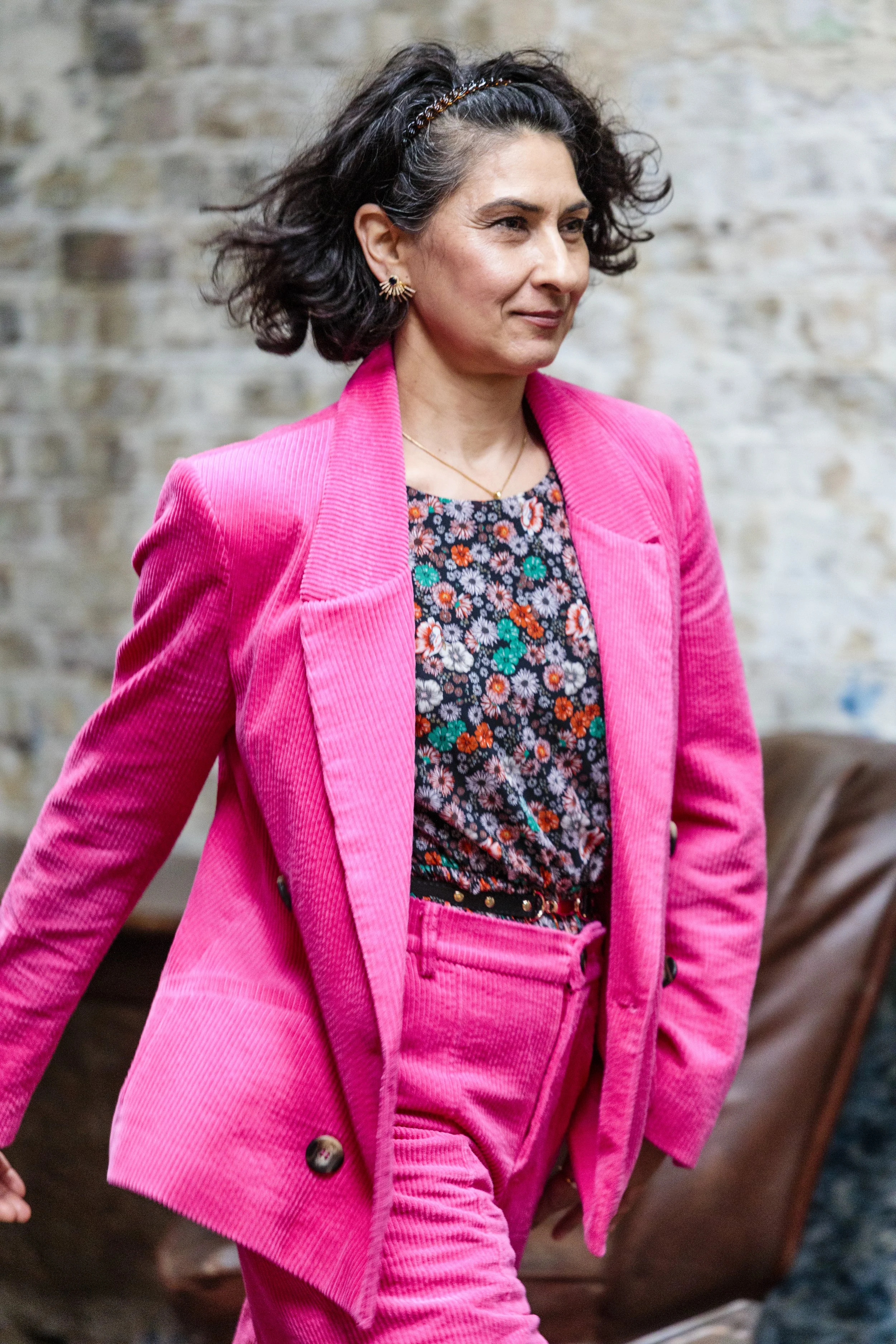 Woman in a bright pink suit with a floral shirt walking indoors.
