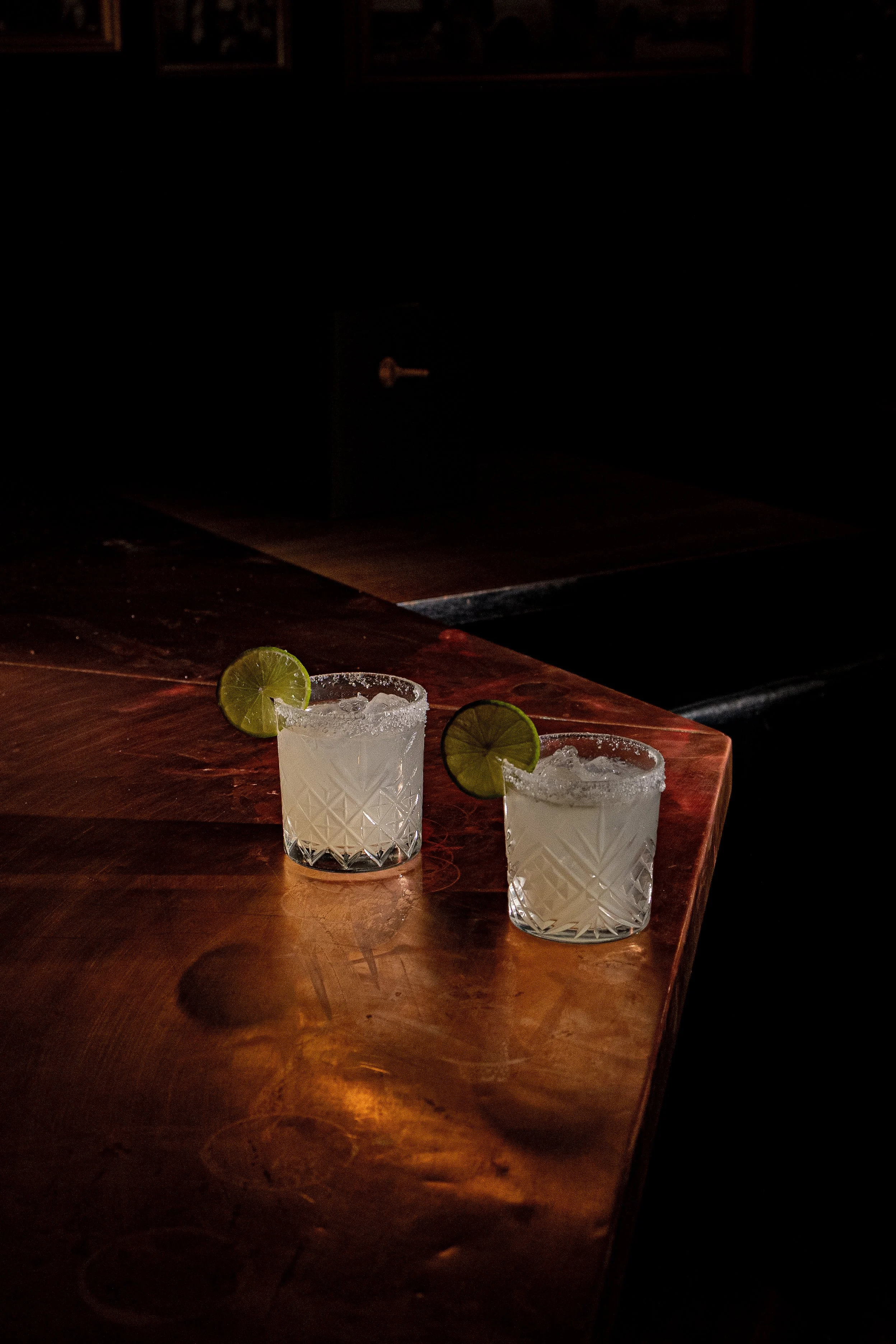 Two cocktails with lime wedges on a wooden bar counter