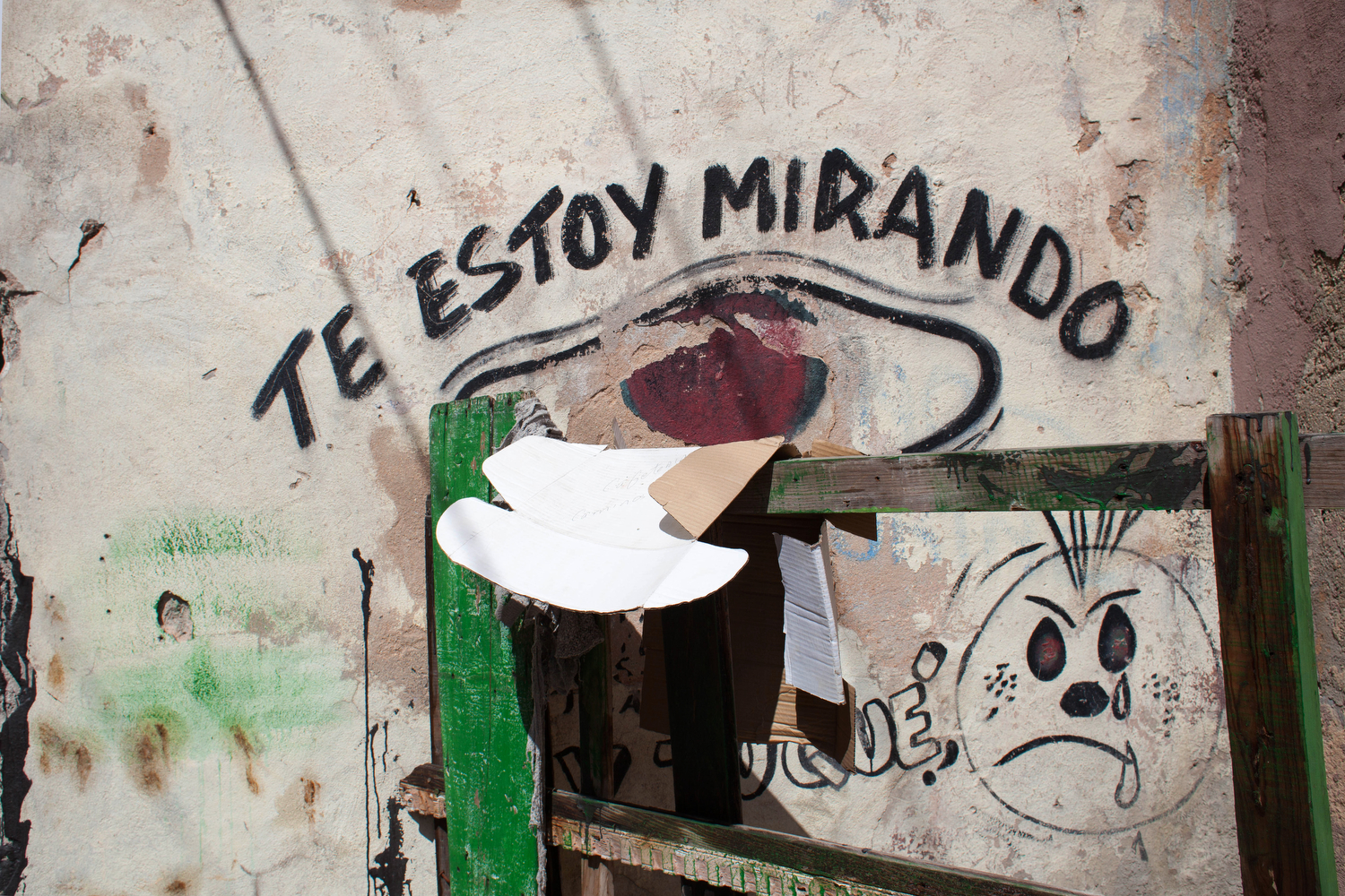  'I Am Watching You' is spray painted on the side of a building near a cobble stoned foot path in downtown Santiago de Cuba. 