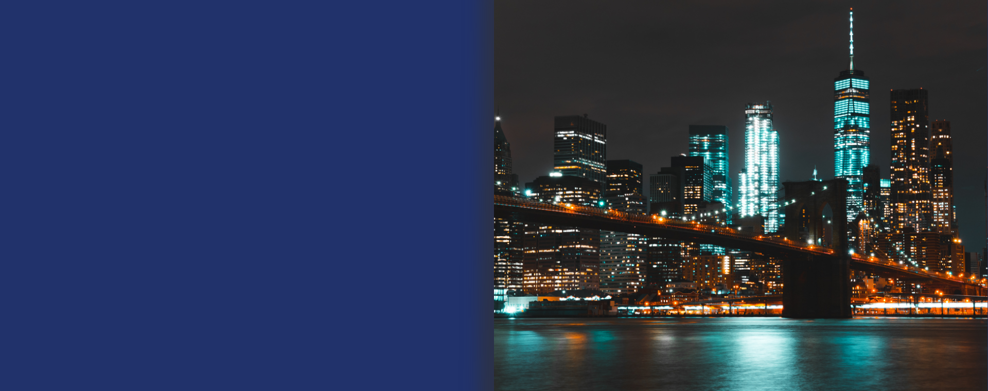 Night view of downtown New York City skyline with illuminated buildings and Brooklyn Bridge over the water.