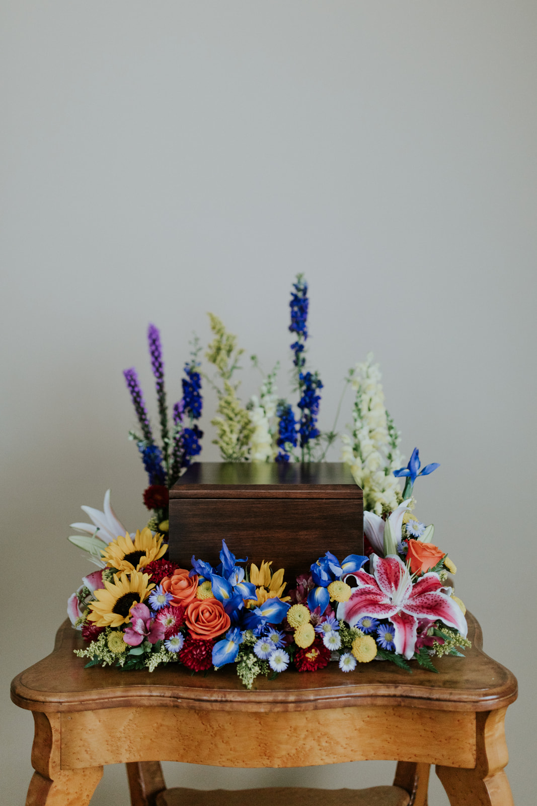  From the Palette Collection, this memorial urn arrangement is designed using a 18-inch square flower frame. Flowers include sunflowers, stargazer lilies, iris, liatris, larkspur, snapdragons, roses, and accent flowers. 