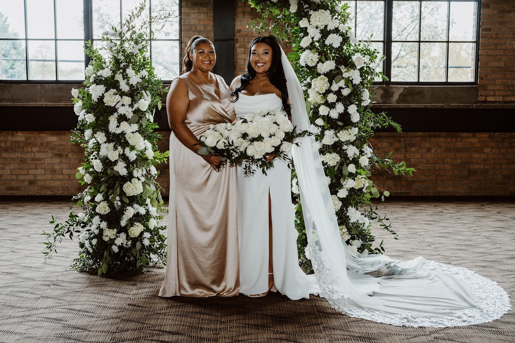 Bride and Bridesmaid holding bouquets of white roses in front of broken arch