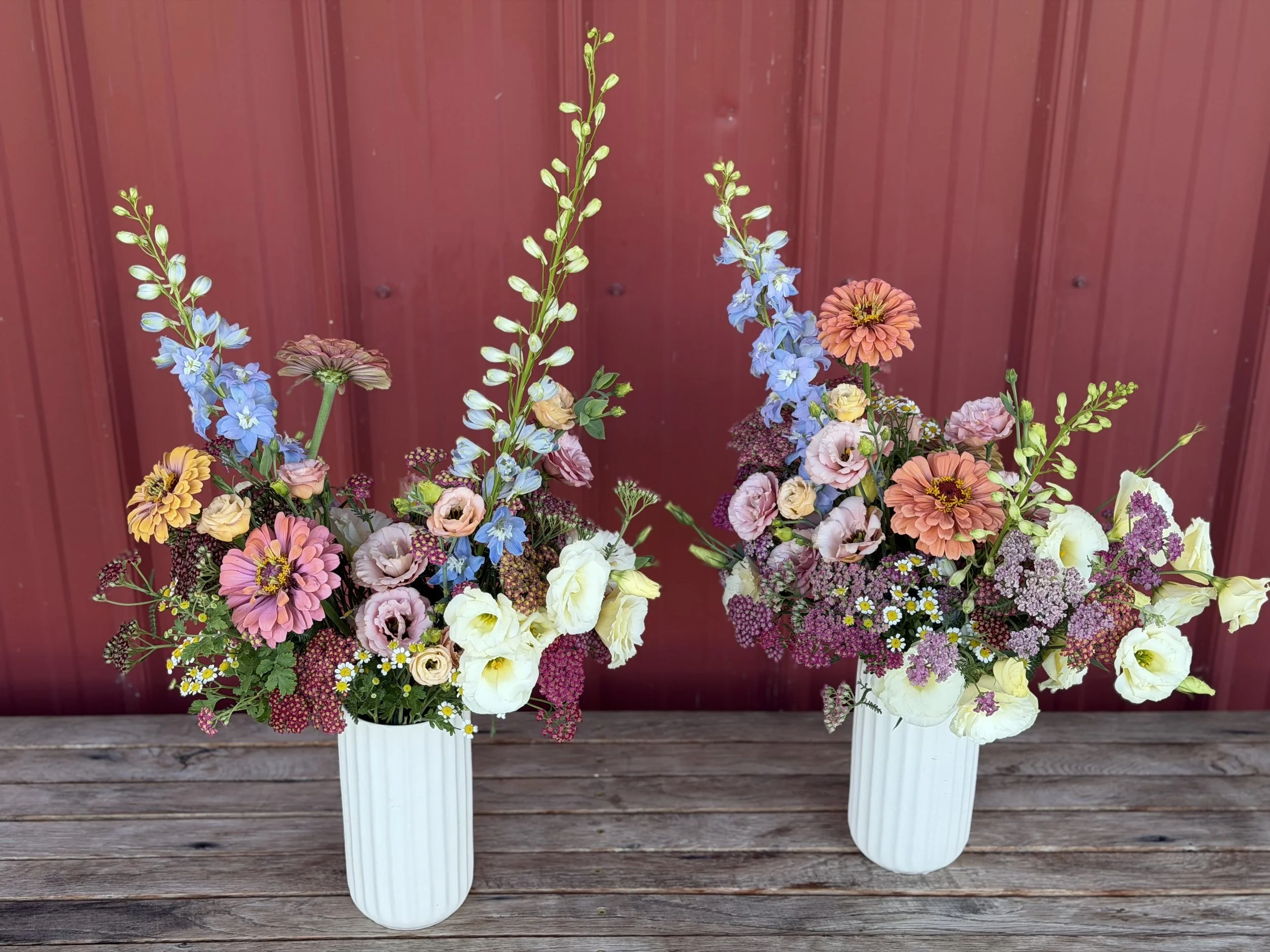 A bouquet of assorted flowers in two ceramic vases, placed on a wooden surface with a red background.