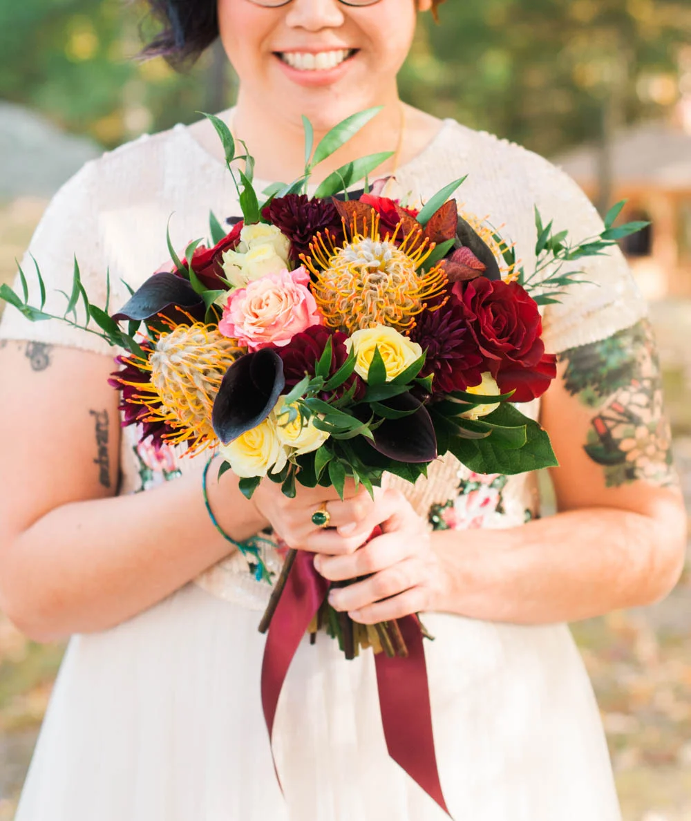 Ephemera Designs Bride holding Amber & Burgundy Bridal Bouquet with Red Ribbon Attached