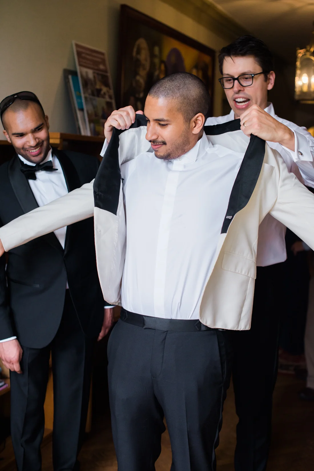 Ephemera Designs Two Groomsmen Help Groom put on Wedding Suit Jacket