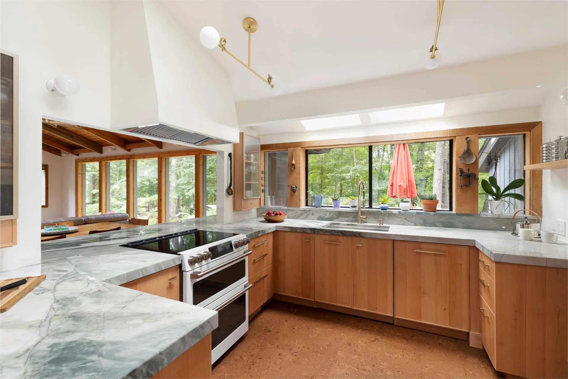 Modern kitchen with wood cabinets and stone countertop. There is a brown cork floor and large windows as well as a concealed range hood.