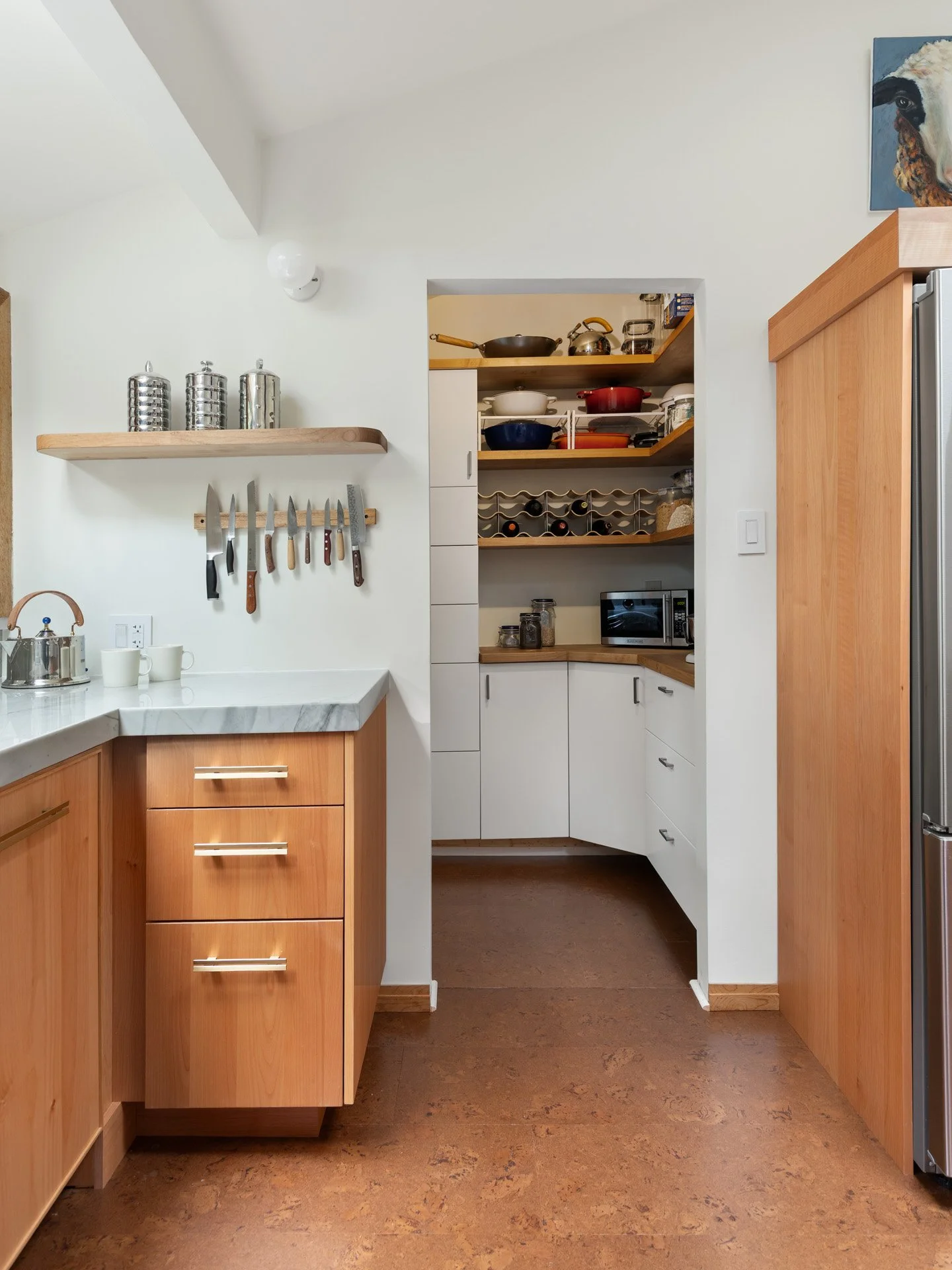 View from modern kitchen into pantry. Kitchen cabinetry matches alder wood floating shelves in pantry and on wall.
