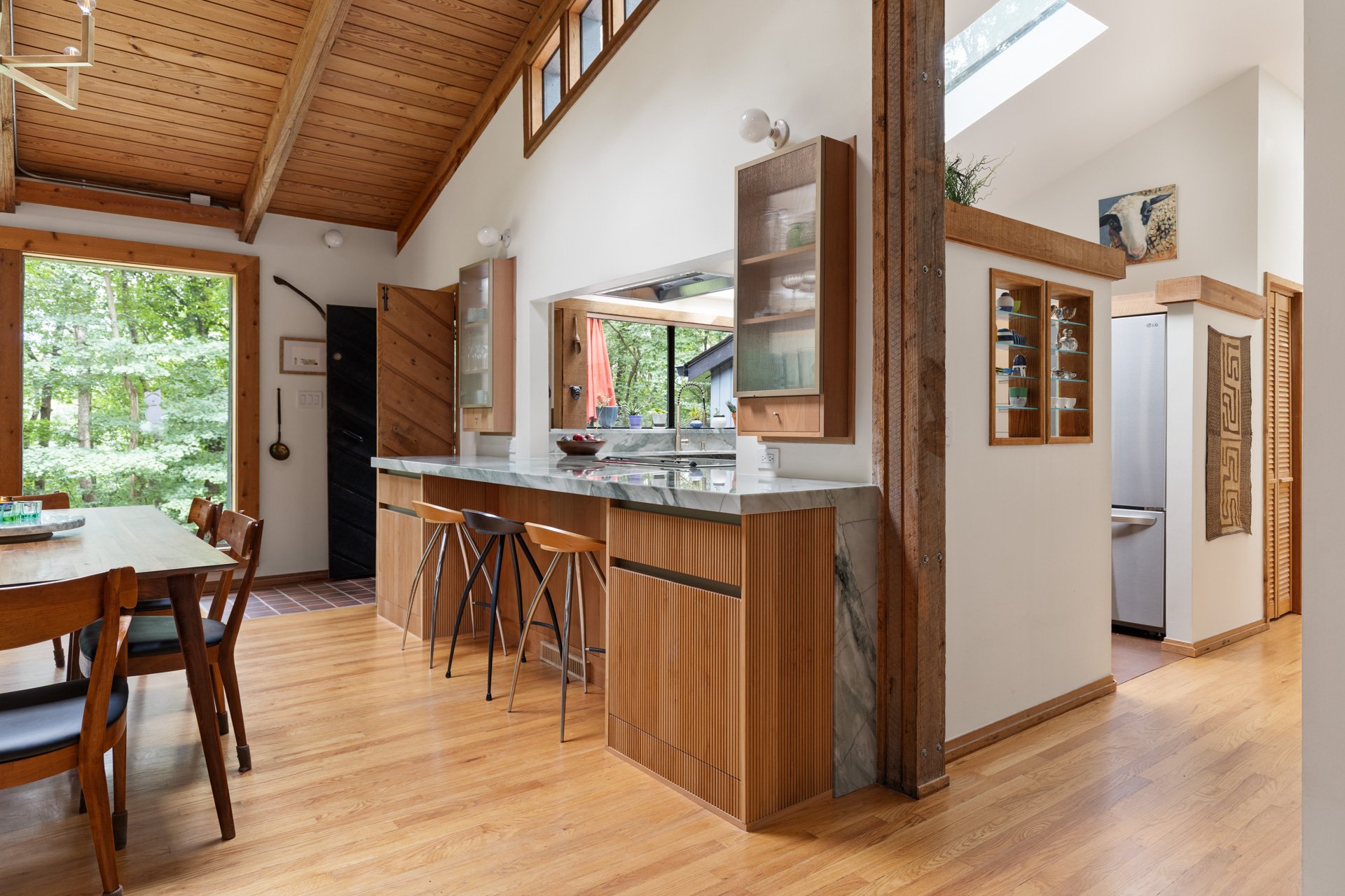 Great room cabinetry with natural wood cabinets and thickened quartzite countertop. Counter seating with mid-century designer stools. Pass through from dining to kitchen is flanked by two built in cabinets.