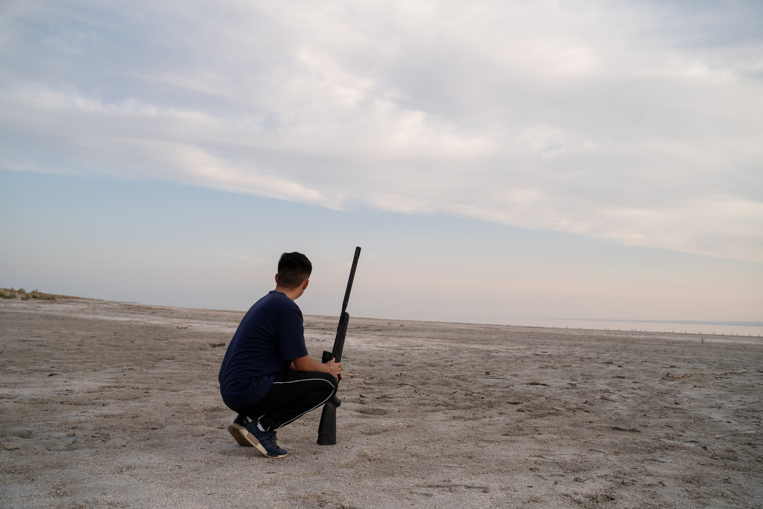 Cesar holds his rifle and looks out onto the Salton Sea.