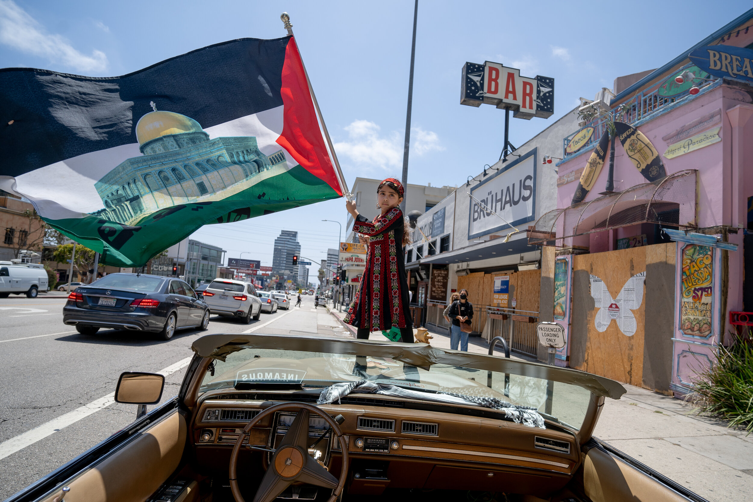 A girl stands on the hood of a convertible and waves a flag during a Palestinian protest in Brentwood.