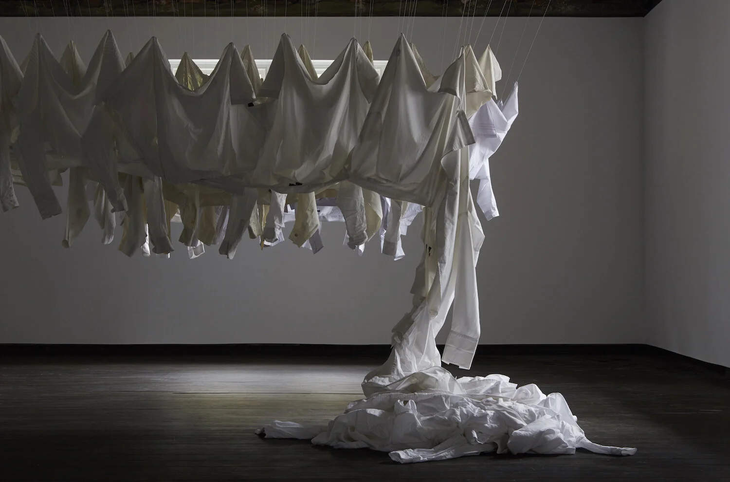 James Nguyen,  Approximately Fifty white shirts buttoned up and organized in shades of white , 2017, cotton thread and shirts, dimensions variable, installation view,  Of All Others , 2017, curated by Kate Britton, Firstdraft, Sydney. Photo: Zan Wimberley. Courtesy the artist.