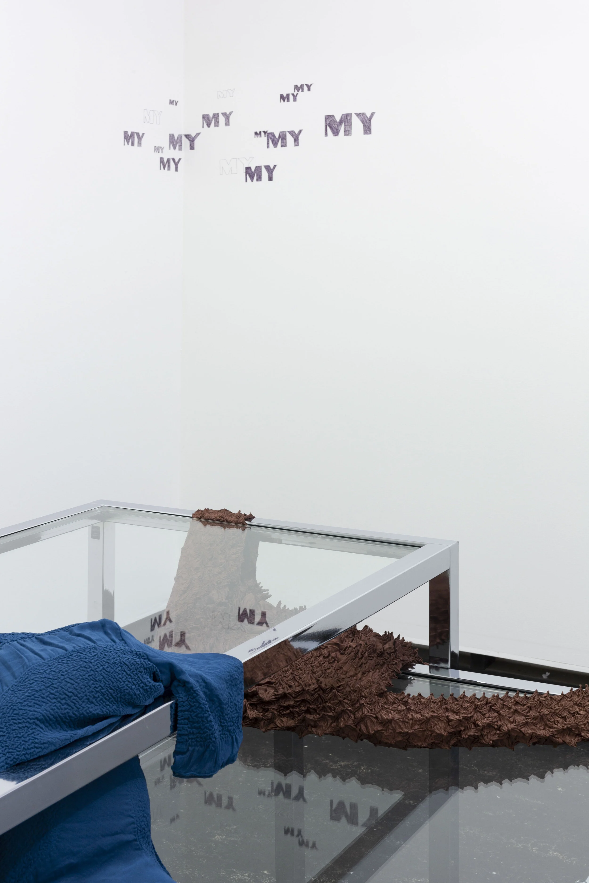 Lill Colgan,  Garment Must Be Handled Delicately, Pulled to Shape, Hand Squeezed , 2020, chrome nesting tables, dressing room hook, second-hand garments, rice, and essential oils, dimensions variable, (foreground);  Benefit Denial , 2020 black biro wall drawing 29.7 × 42 cm (background), installation view (detail),  A Hole Where There Once Was A Logo , 2020, Firstdraft, Sydney. Photo: Jessica Maurer. Courtesy the artist.