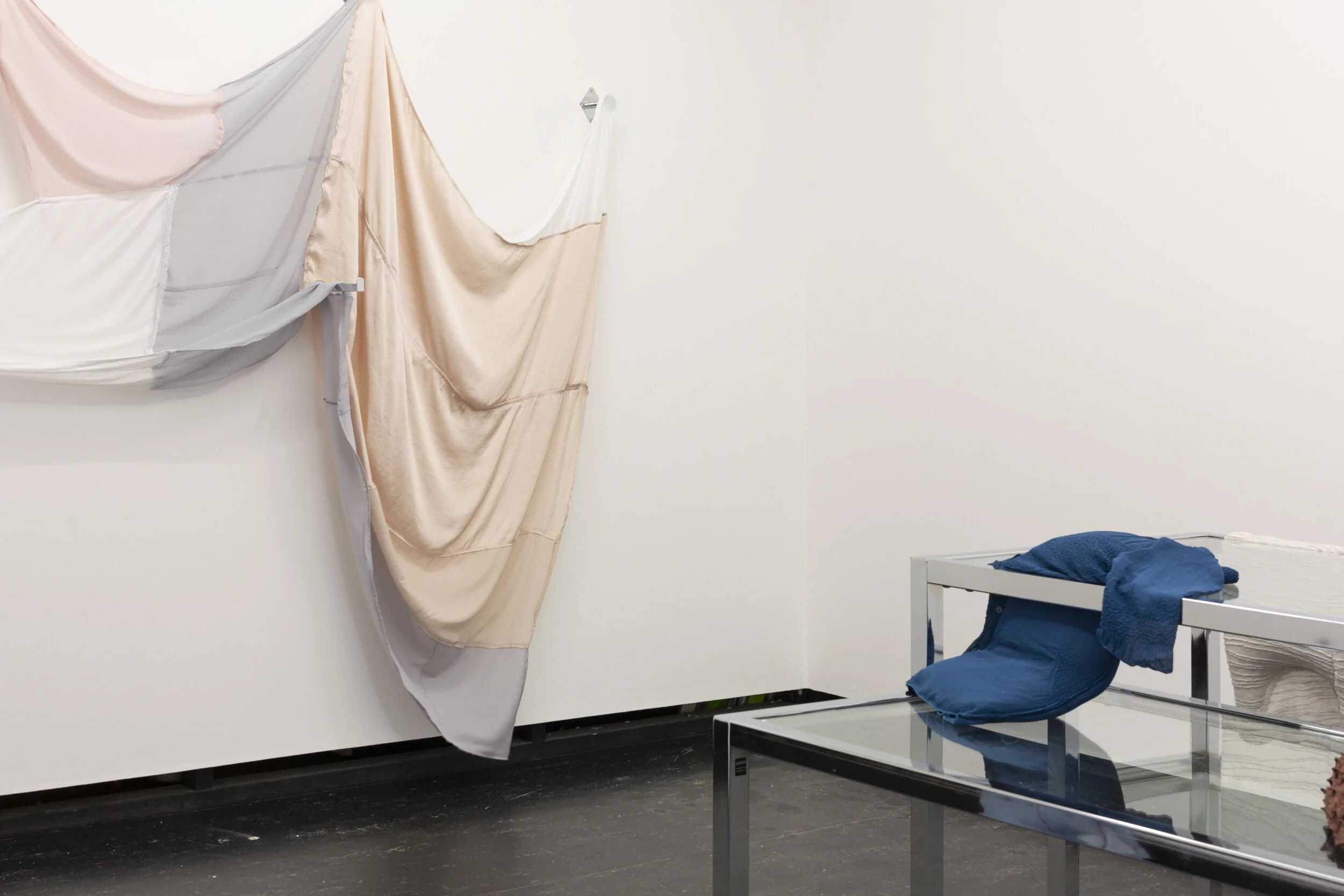 Lill Colgan,  Girl Introjected , 2020 various second-hand garments, nail polish, dressing room hooks and straight arm hanging rail, dimensions variable, (background);  Garment Must Be Handled Delicately, Pulled to Shape, Hand Squeezed , 2020, chrome nesting tables, dressing room hook, second-hand garments, rice, and essential oils, dimensions variable (foreground), installation view (detail),  A Hole Where There Once Was A Logo , 2020, Firstdraft, Sydney. Photo: Jessica Maurer. Courtesy the artist.