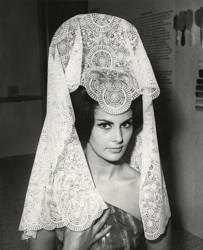 Model Eileen Noble met een kunststof tafelkleed gedragen als een mantilla op een tentoonstelling van kunststof. Londen, 1963. Plastic table cloth worn as a mantilla by model Eileen Noble. London,1963.