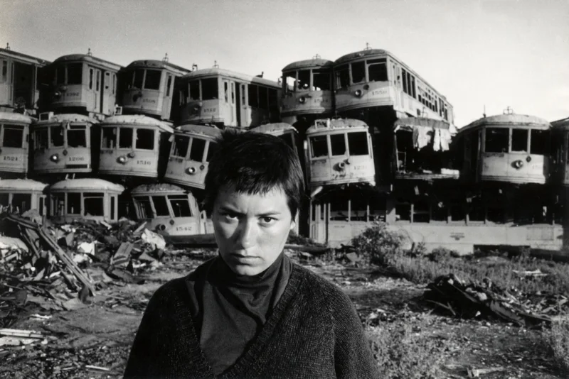 De wereldreis van Gerda en Ed van der Elsken. Een jongen poseert voor een enorme stapel oude treinwagons op een opslagplaats van oud roest. Verenigde Staten van Amerika, Los Angeles, 1960. Foto: Ed van der Elsken. The trip around the world of Gerda and Ed van der Elsken. A boy posing in front of a gigantic heap of old streetcars at a junk yard. United States of America, Los Angeles, 1960.