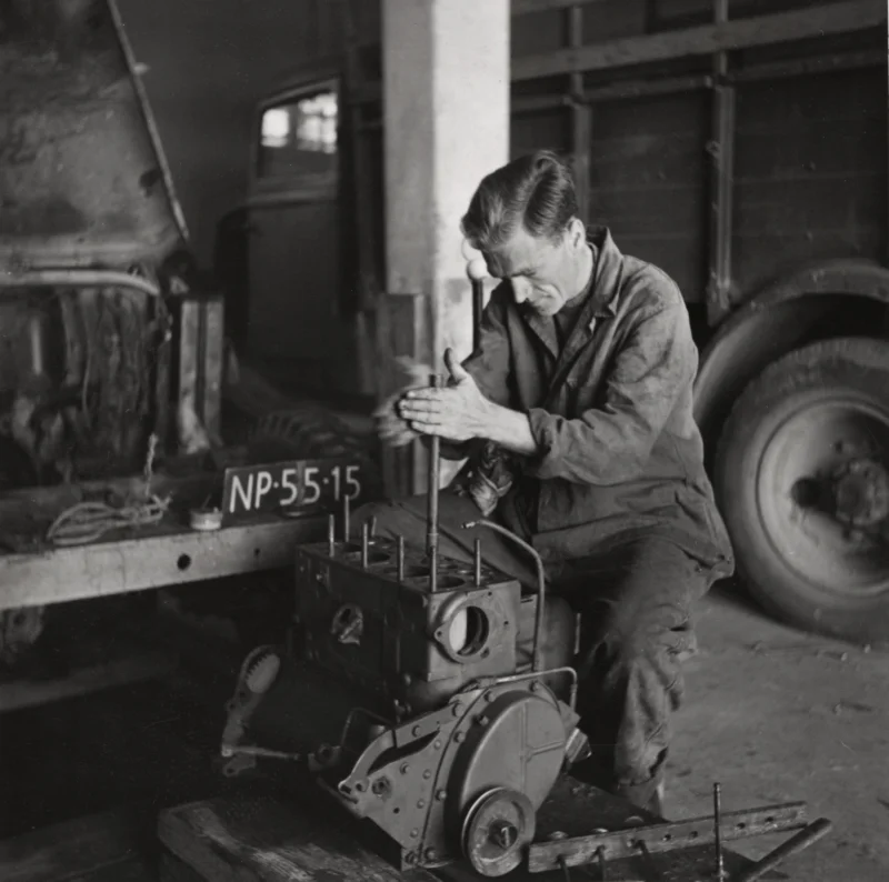 Fotograaf Peter Pennarts heeft de motor van de jeep uit elkaar gehaald. Hij schuurt de verbrande kleppen bij. Libanon, Beiroet, 1954. Photographer Petter Pennarts has taken the engine of the jeep apart. He is sanding the burned valves. Lebanon, Beirut, 1954.