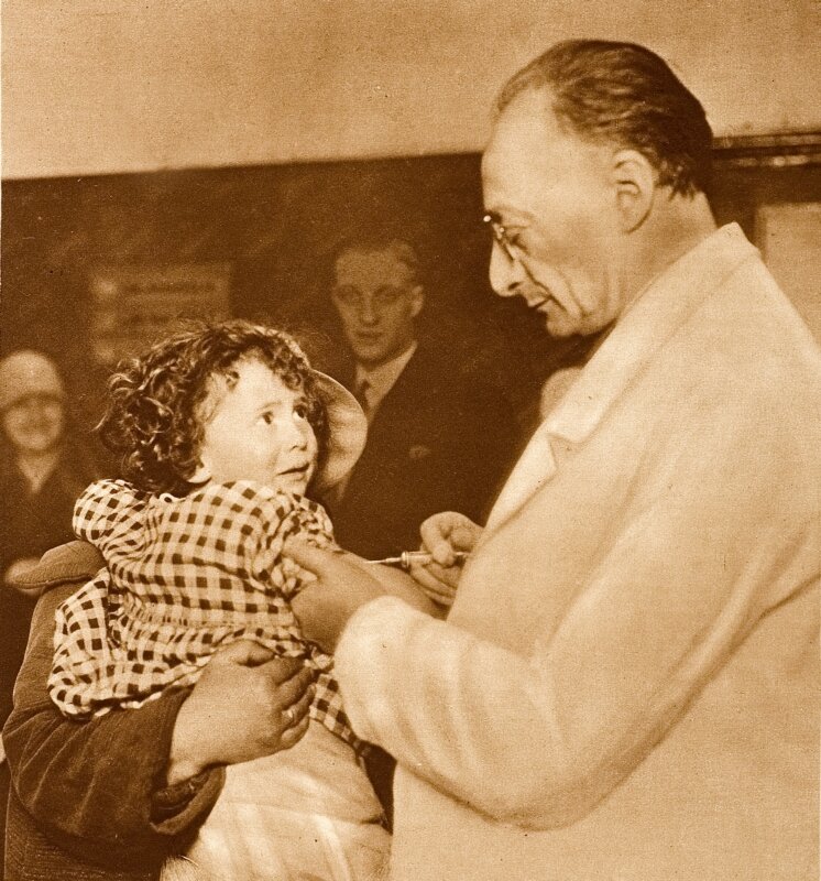  Bij de geneeskundige dienst worden kinderen ingeënt tegen diphterie. Een protesterende baby zit op de arm van haar moeder, terwijl de dokter met de injectienaald het serum inspuit. april 1929. 