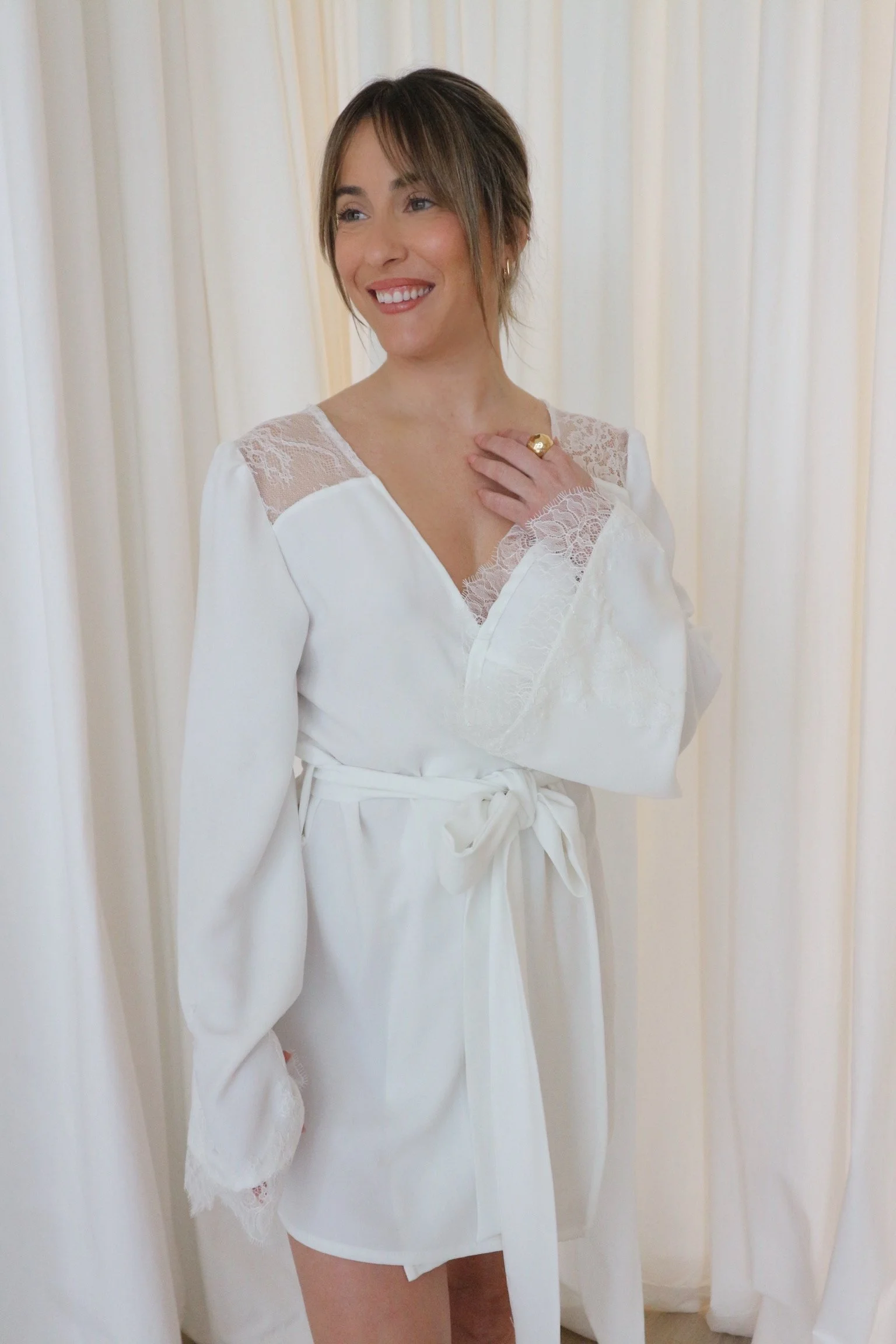 Mujer sonriendo con bata de satén blanca, rodeada de cortinas blancas.