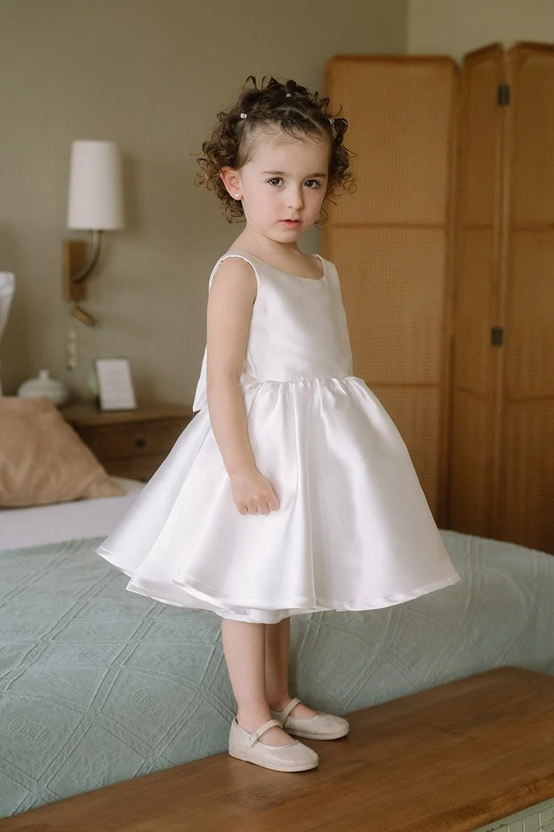 Niña vestida con vestido blanco y zapatos, en una habitación.