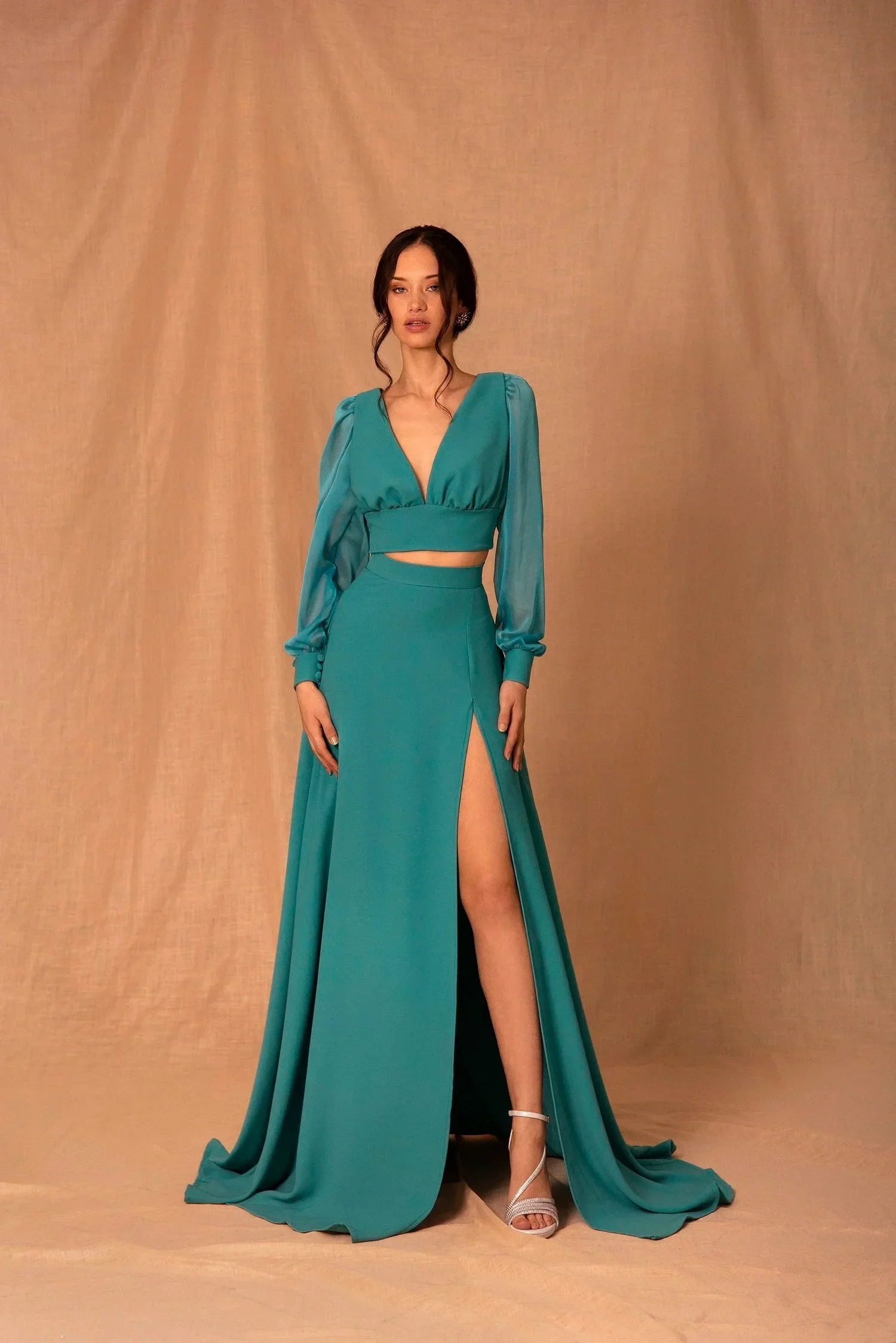 Mujer con vestido largo y falda con abertura en la pierna, de color turquesa, en un fondo beige