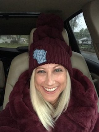 A women wearing the chunky cable knit beanie style stocking hat with pom on top.  burgundy hat with an embroidered Wisconsin rivers patch.