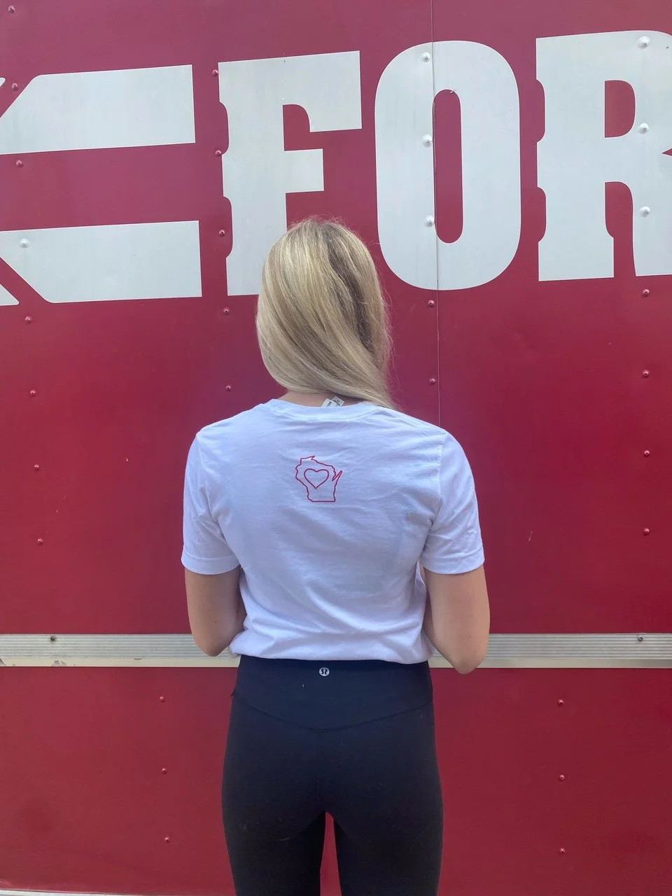 A girl showing the back of a sueded cotton unisex white tshirt with Wisco INTL screen printed graphic featuring Jumping Badger in the Puma style.