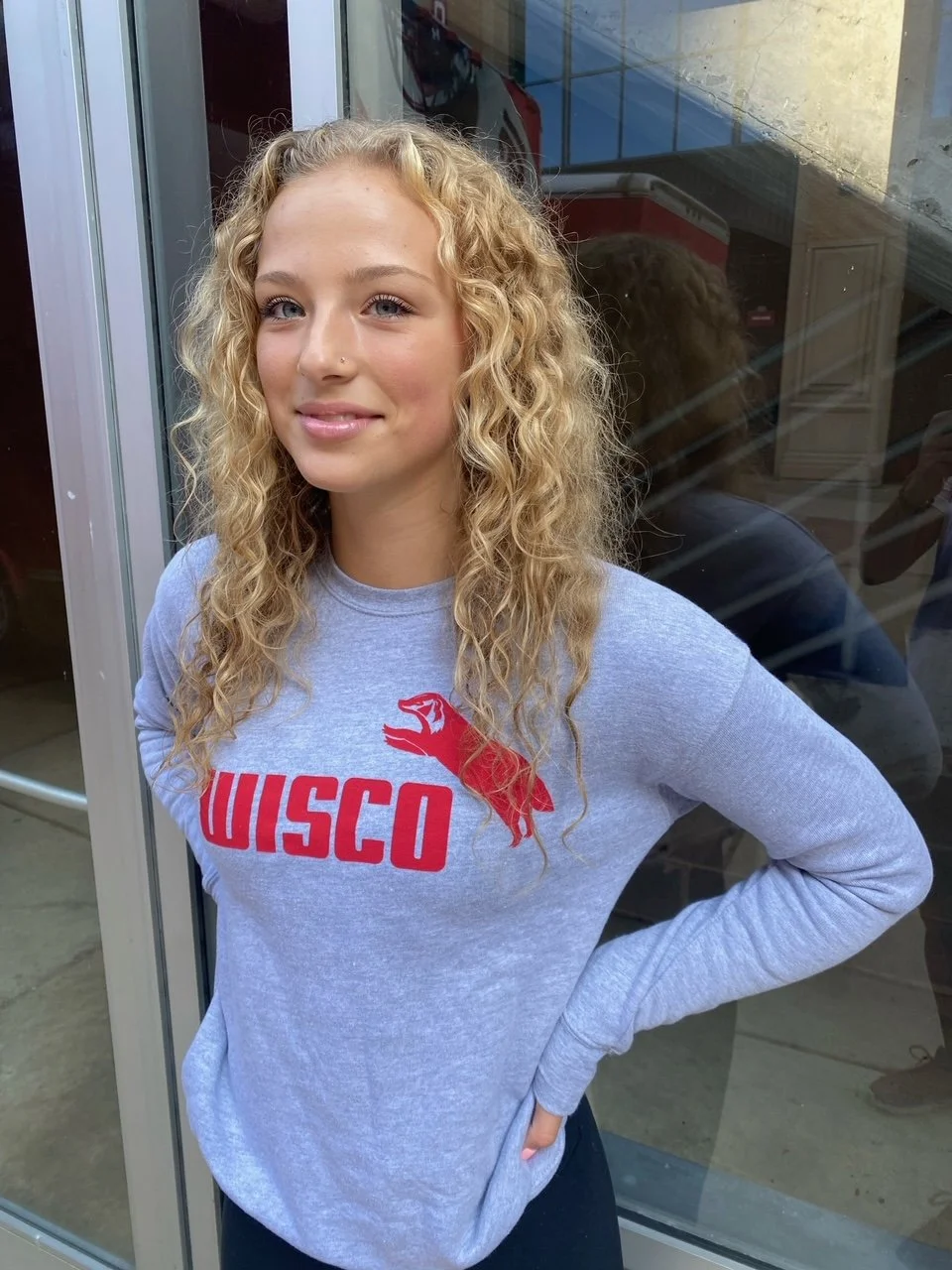 A young woman wearing the unisex crewneck sweatshirt in classic athletic heather grey with Wisco INTL screen printed graphic featuring Jumping Badger in the Puma style.