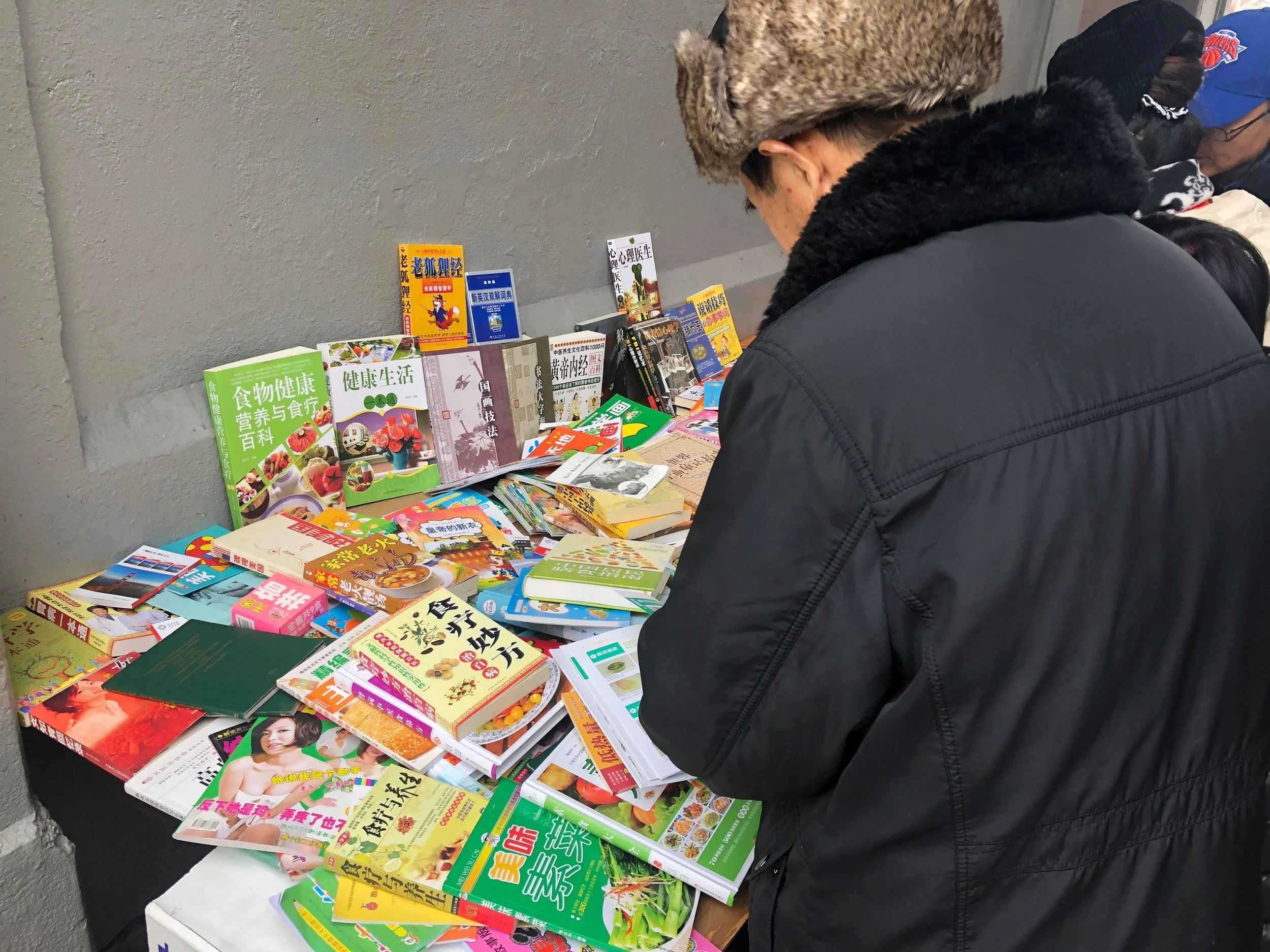 Man looking at books for sale on Main St, Flushing, Queens.