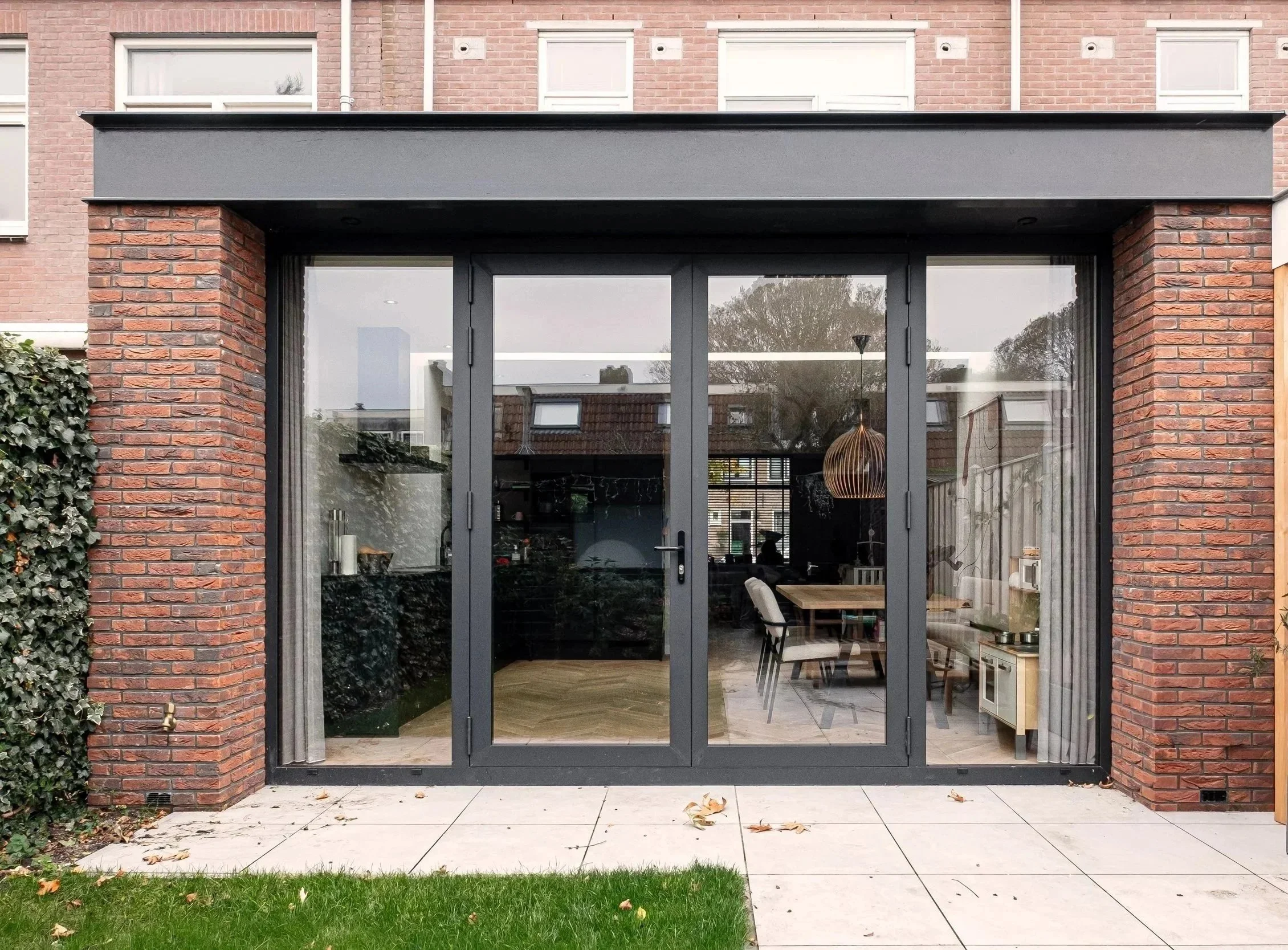 Front view of a modern house with glass sliding doors, a brick exterior, and a small patio with a grass patch and tiled walkway.