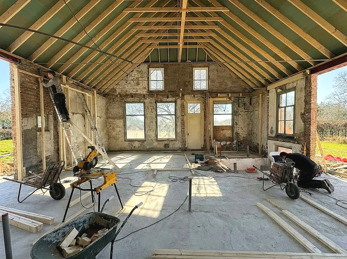 Interior of a house under renovation with construction tools and workers installing wall framing and ceiling beams.