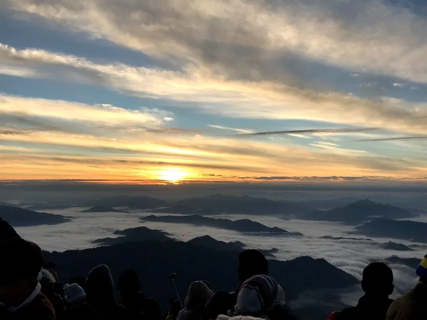 7:00 AM - The sun peaks over the horizon above a sea of fog and a crowded audience.