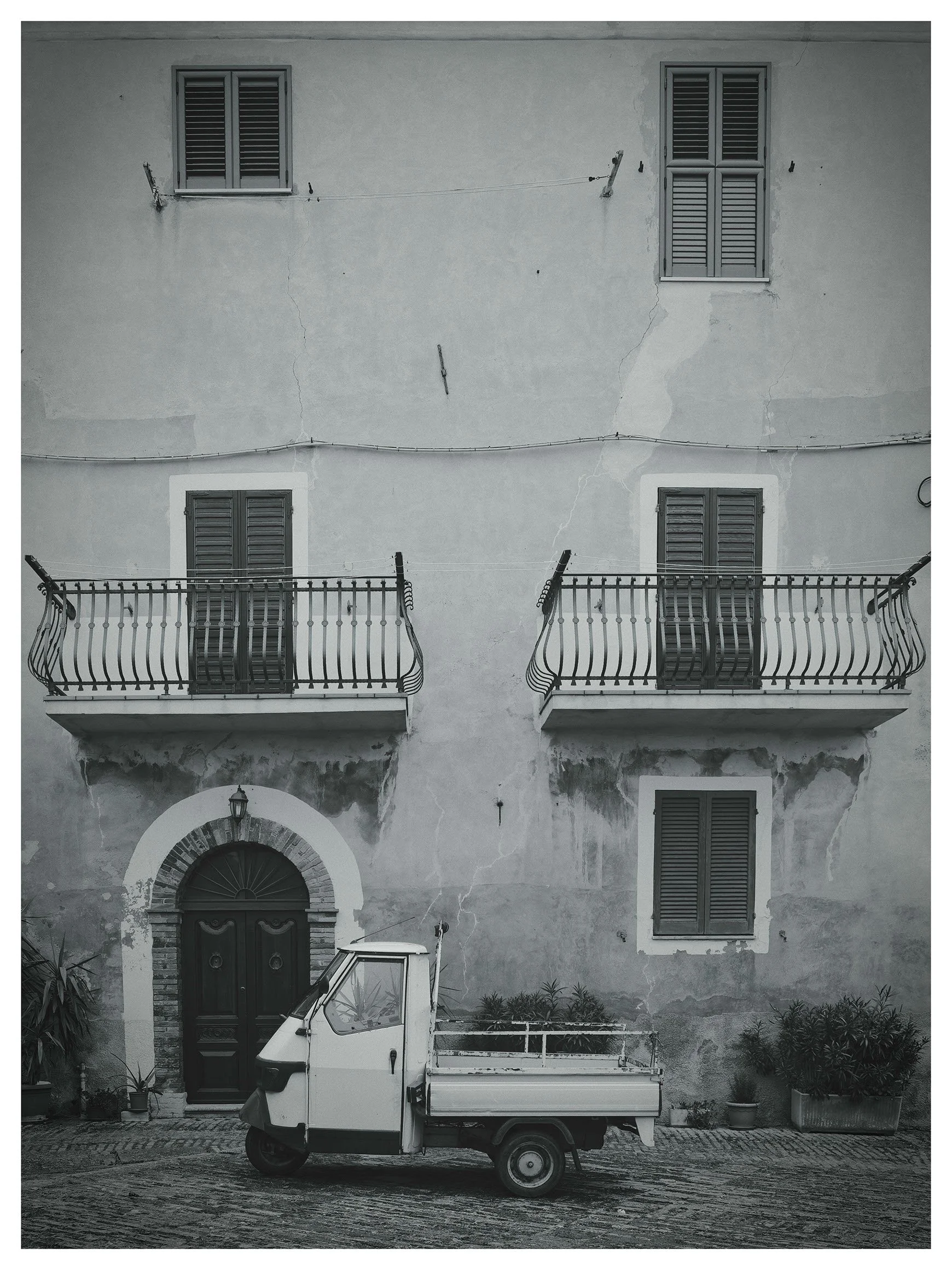 A small utility vehicle parked in front of an old building with cracks in the wall and shuttered windows.
