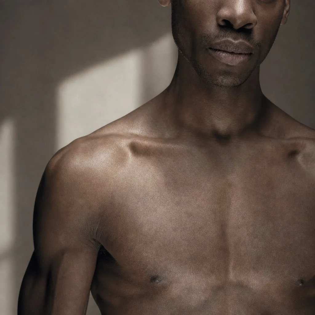 Close-up of a shirtless man's upper body and face, with a shadowed background.