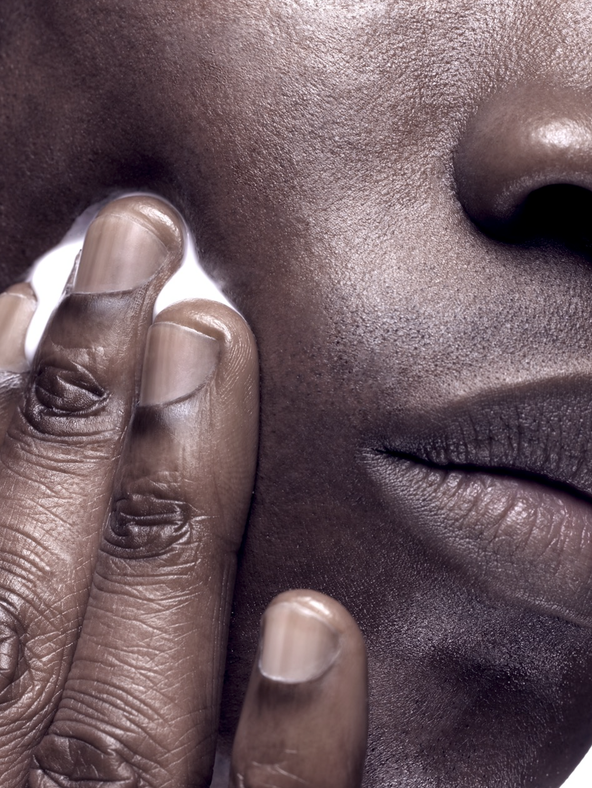 Close-up of a person with dark skin touching their face gently with their fingers.