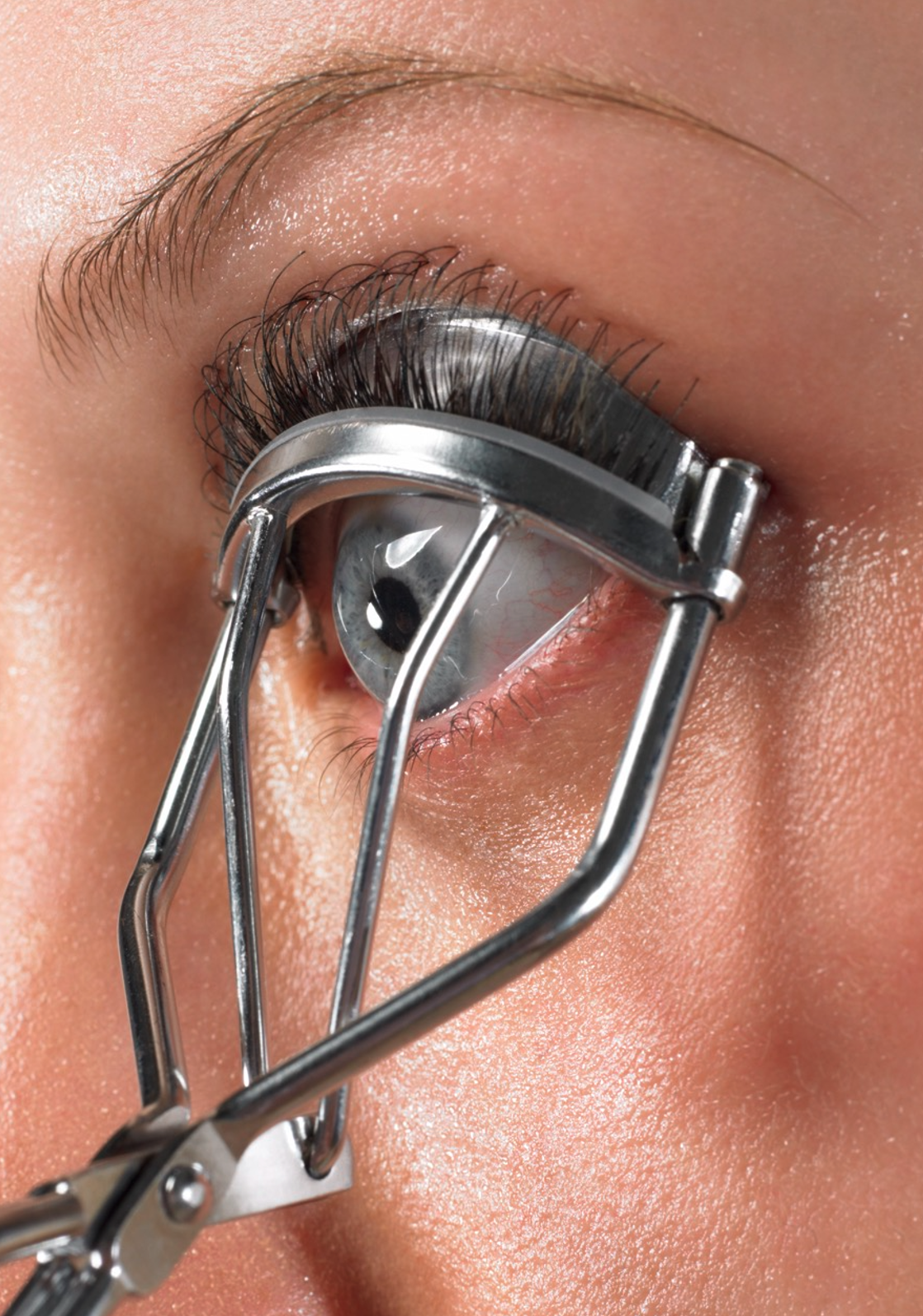 Close-up of a person's eye with eyelash extensions being curled with an eyelash curler.