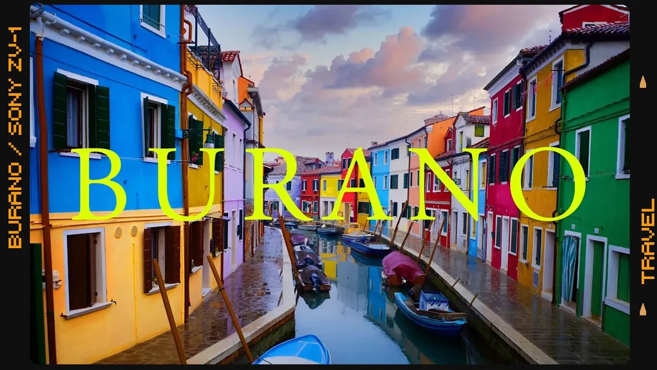 Colorful buildings lining a canal in Burano, Italy, with boats docked along the water and a cloudy sky above.