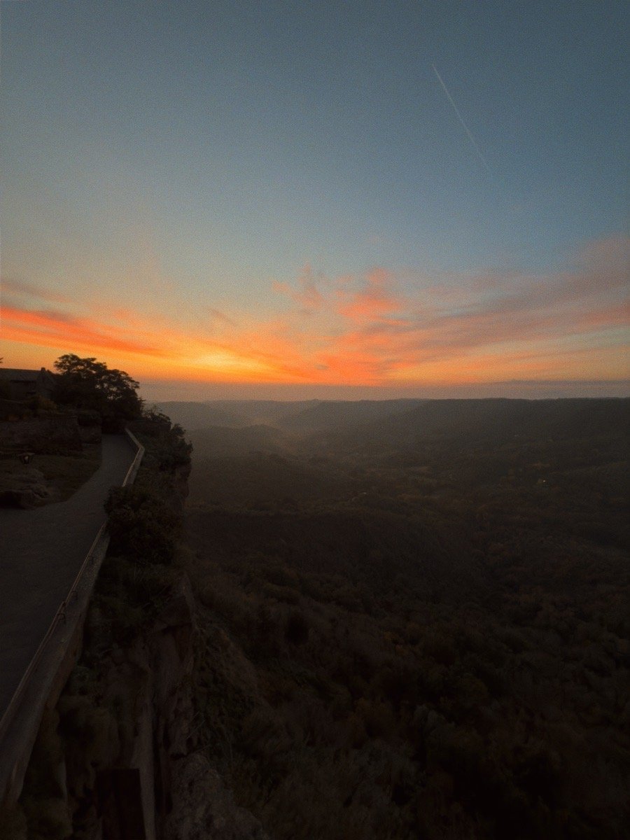Sunset view over a vast landscape with a highway on the left side and a cloudy sky.