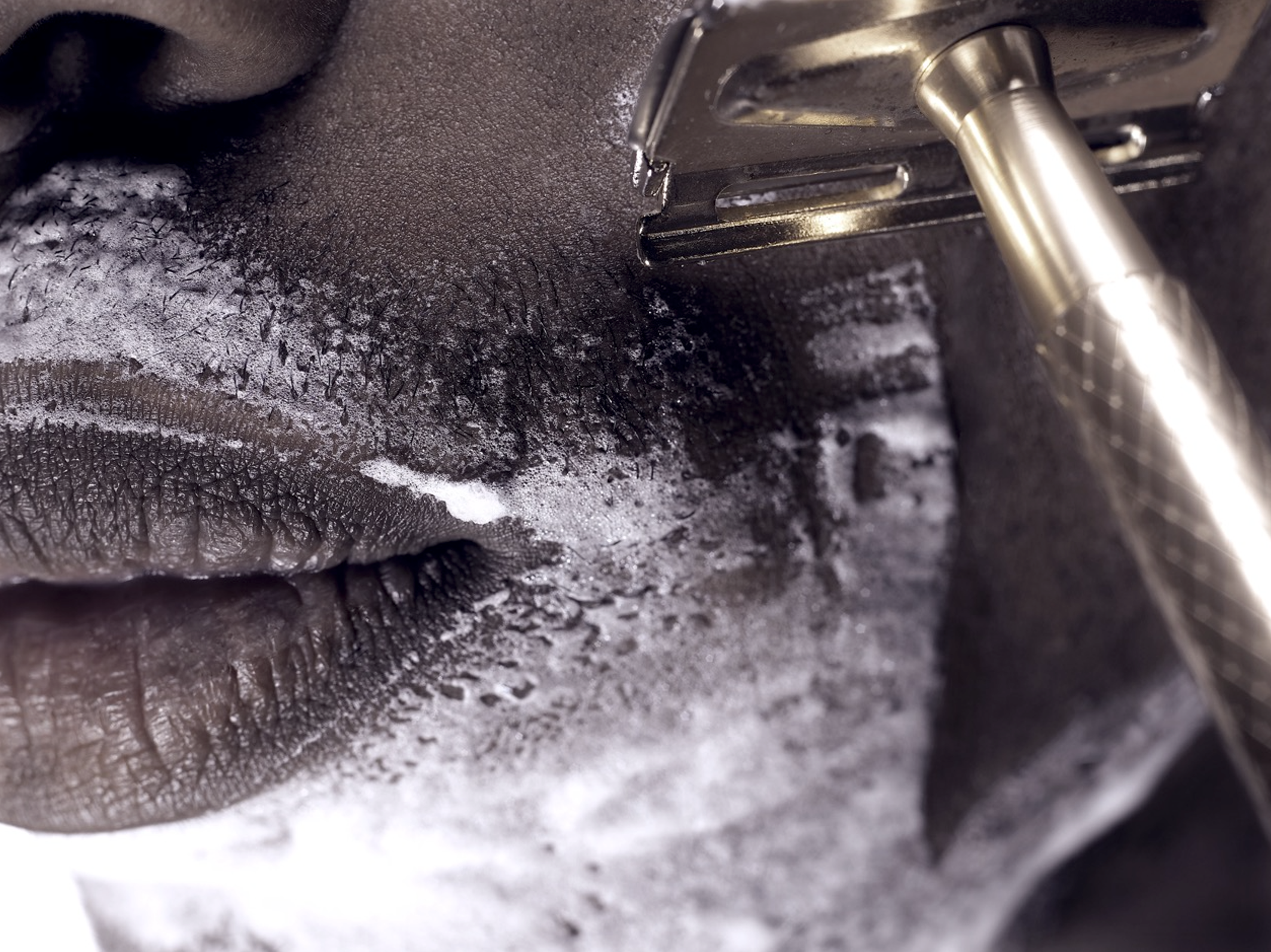 Close-up photo of a metal drilling or grinding bit on a dark metallic surface, with small particles and debris around.