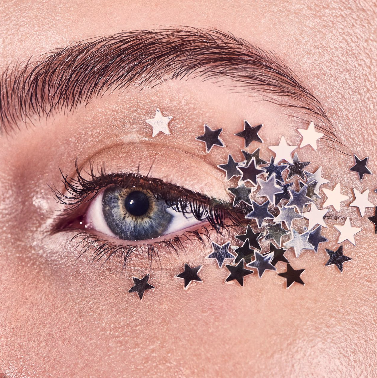 Close-up of a human eye with makeup and scattered silver star-shaped glitter on the eyelid and surrounding skin.