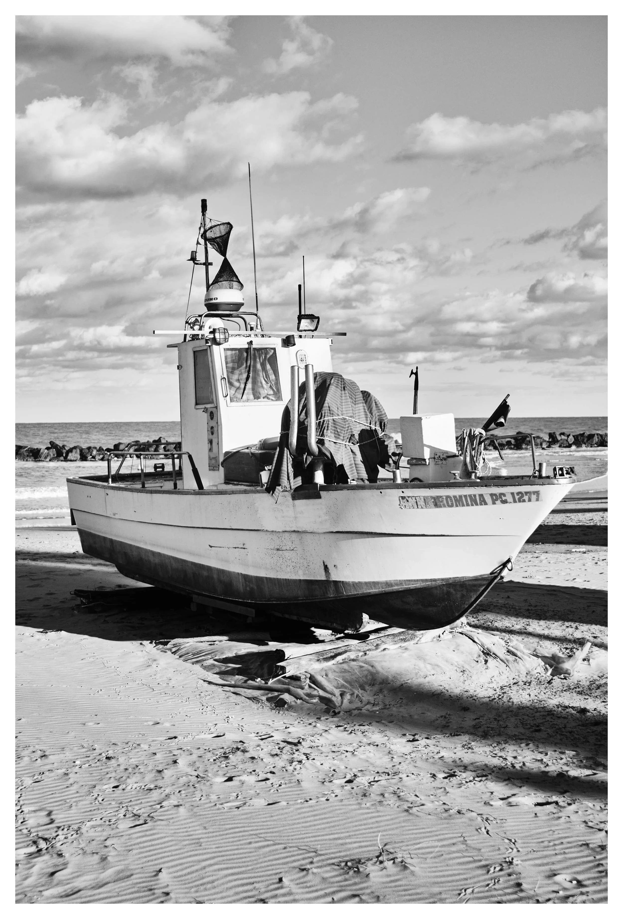 A boat on a sandy beach with the ocean and cloudy sky in the background, black and white coloring.