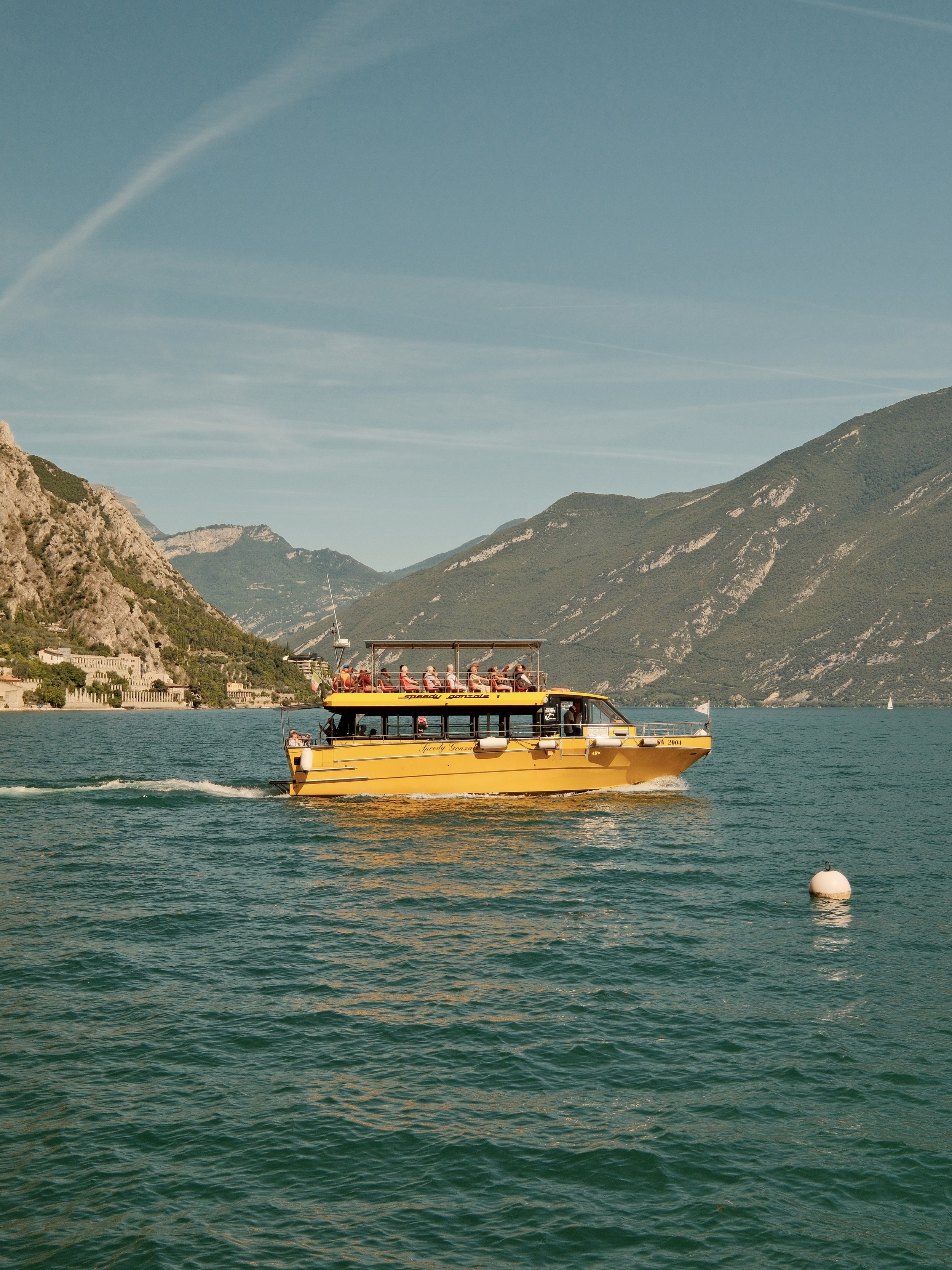 A yellow boat with a covered upper deck carrying passengers on a lake surrounded by mountains.