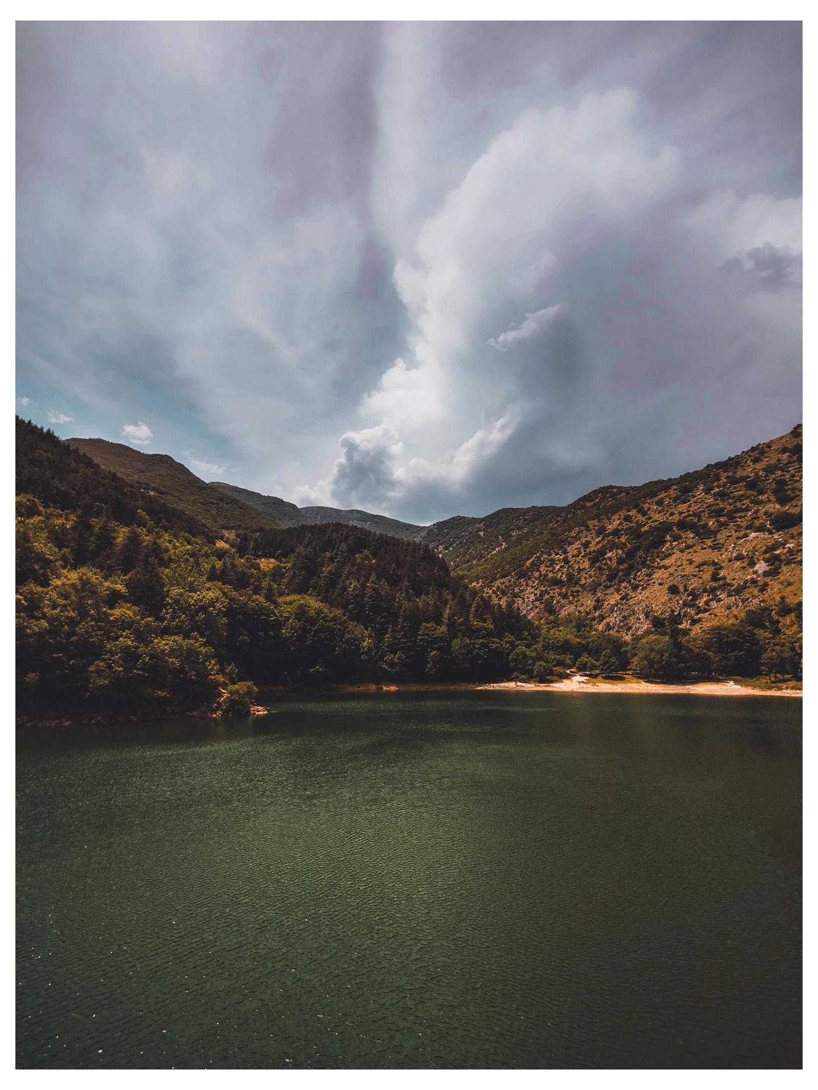 A lake surrounded by forested hills under a cloudy sky.