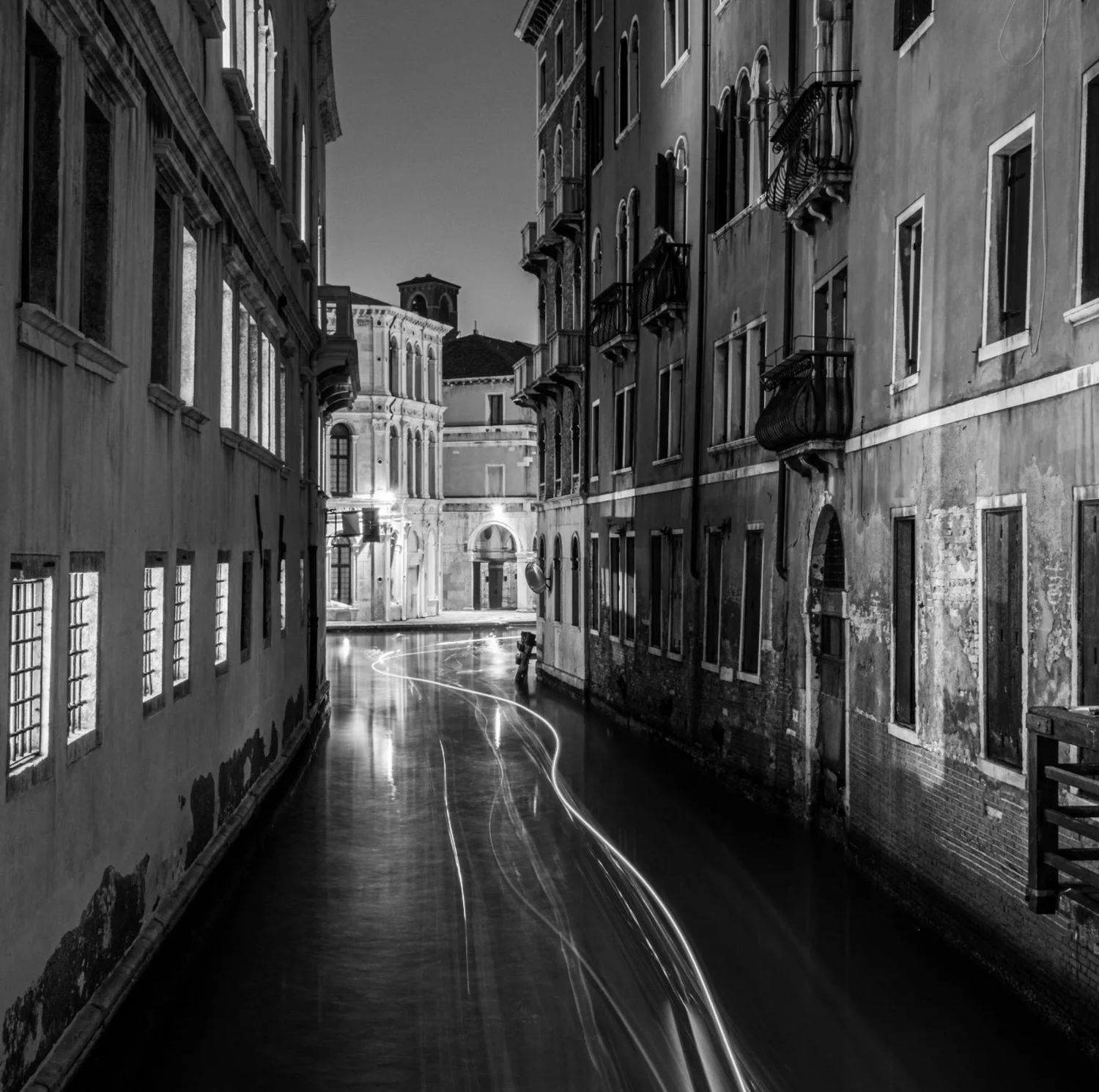 Nighttime view of a canal in Venice, Italy, with historic buildings on either side and light trails on the water from moving boats.