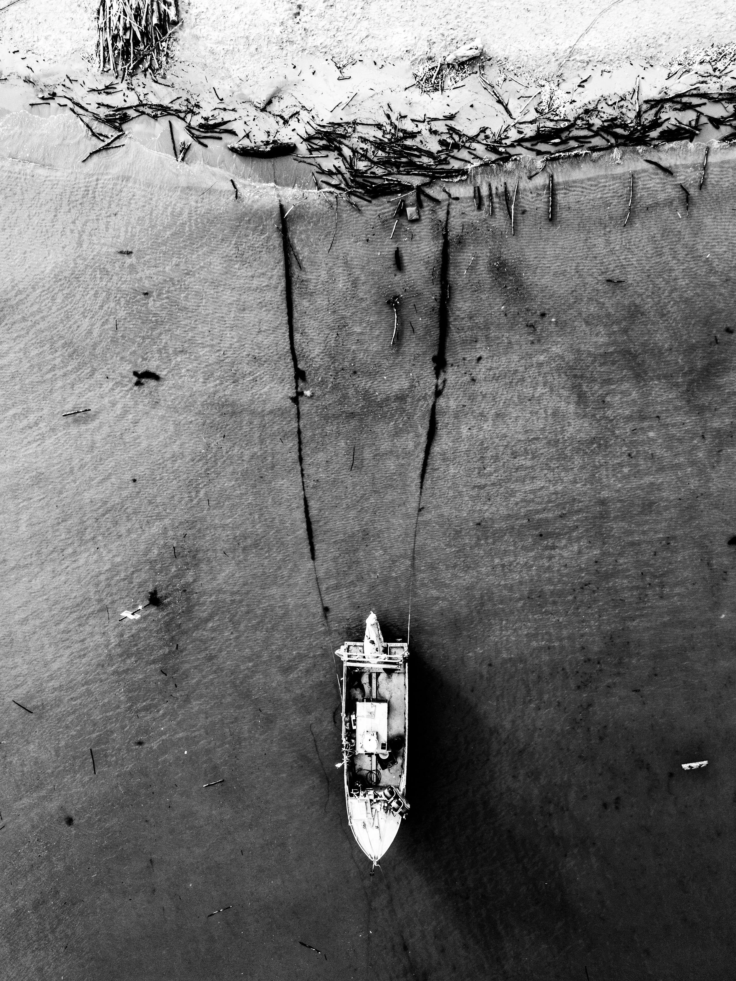 Black and white aerial photo of a shipwreck in shallow water with debris and seaweed nearby.
