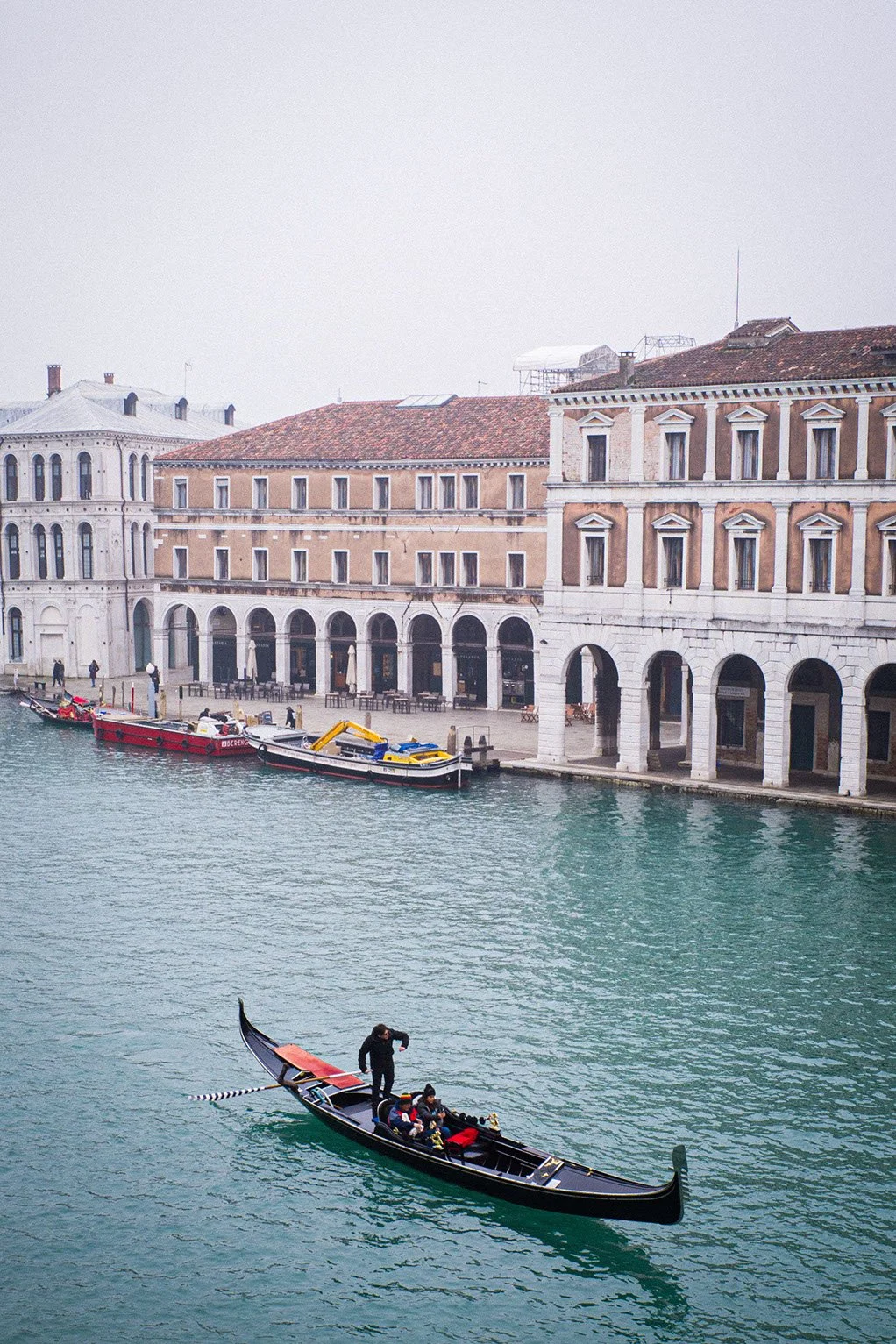 Gondola with three people on a canal in Venice, Italy, with historic buildings and boats docked along the water.