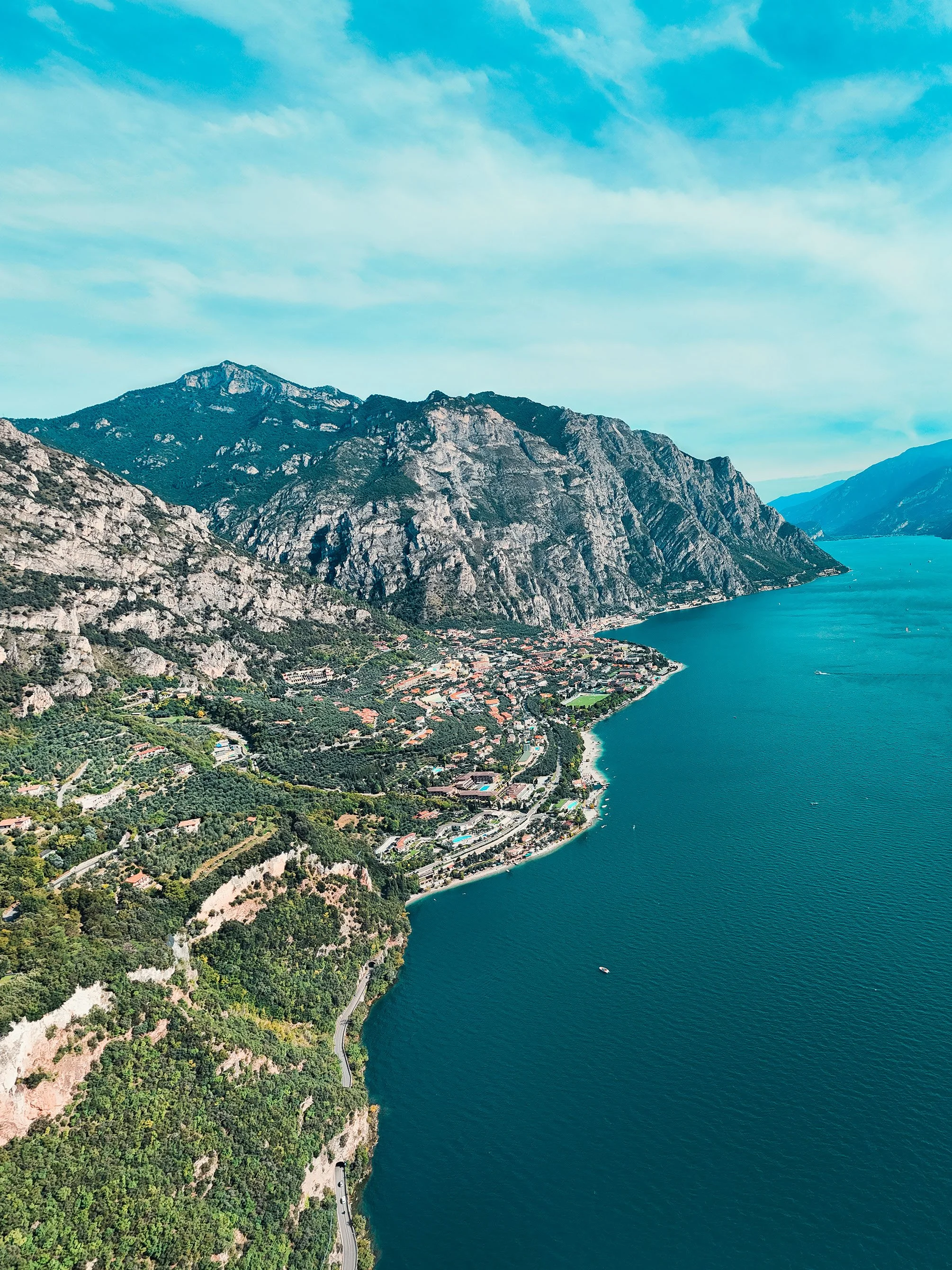 Aerial view of a lakeside town with mountains in the background, clear blue sky, and a calm body of water with a boat.