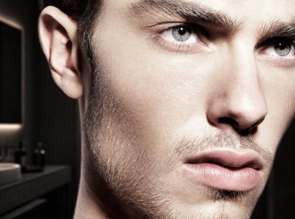 A close-up of a man's face focusing on his blue eyes, eyebrows, and facial hair with a blurred background.