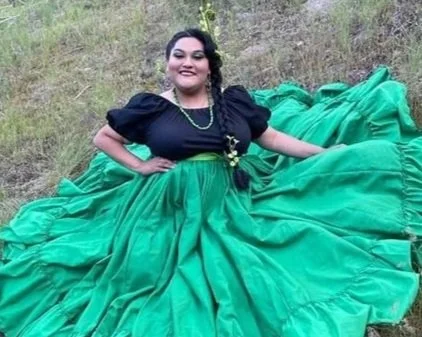 Woman in a black top and green skirt sitting outdoors on grass